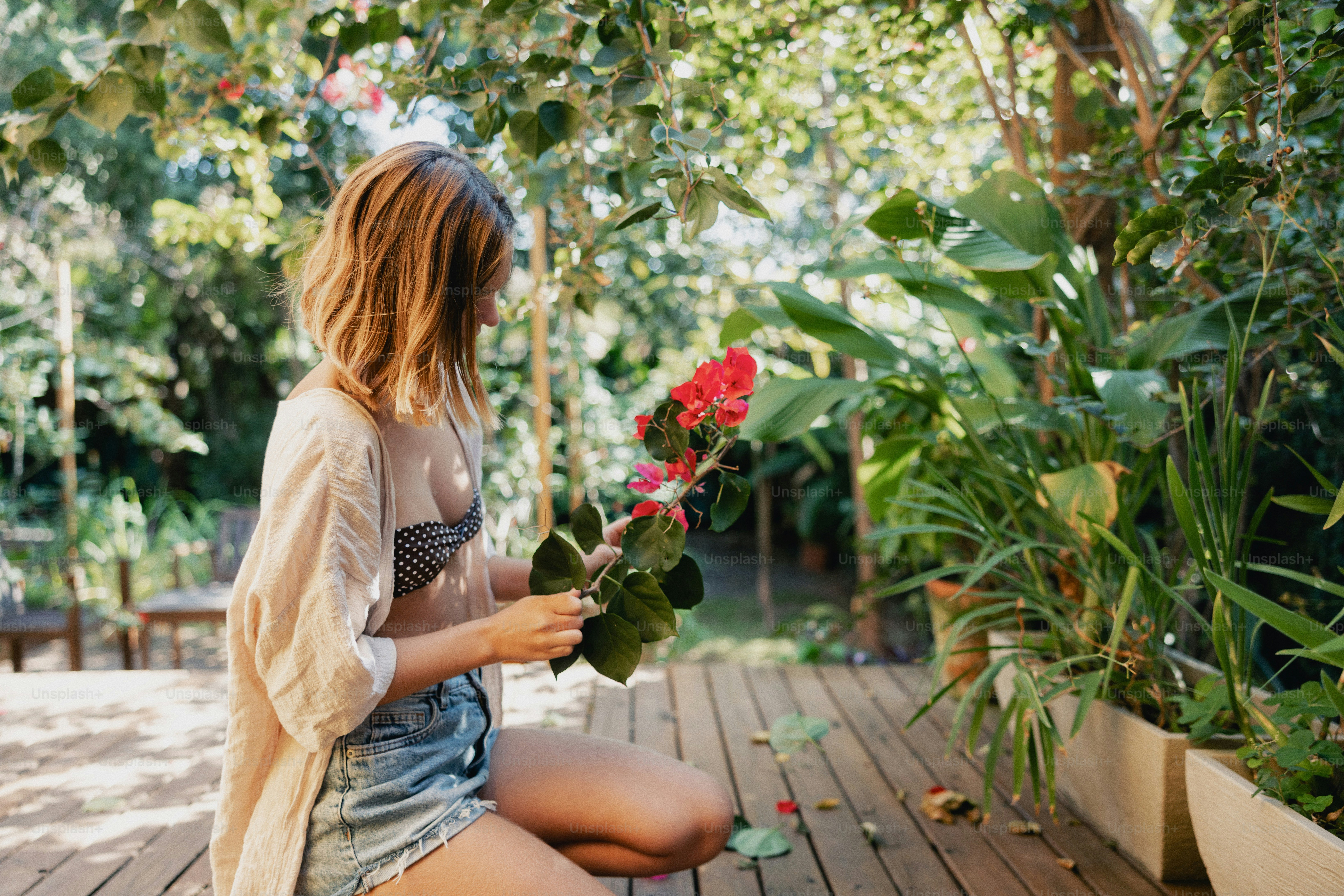 A woman arranges red flowers on a wooden deck outdoors.