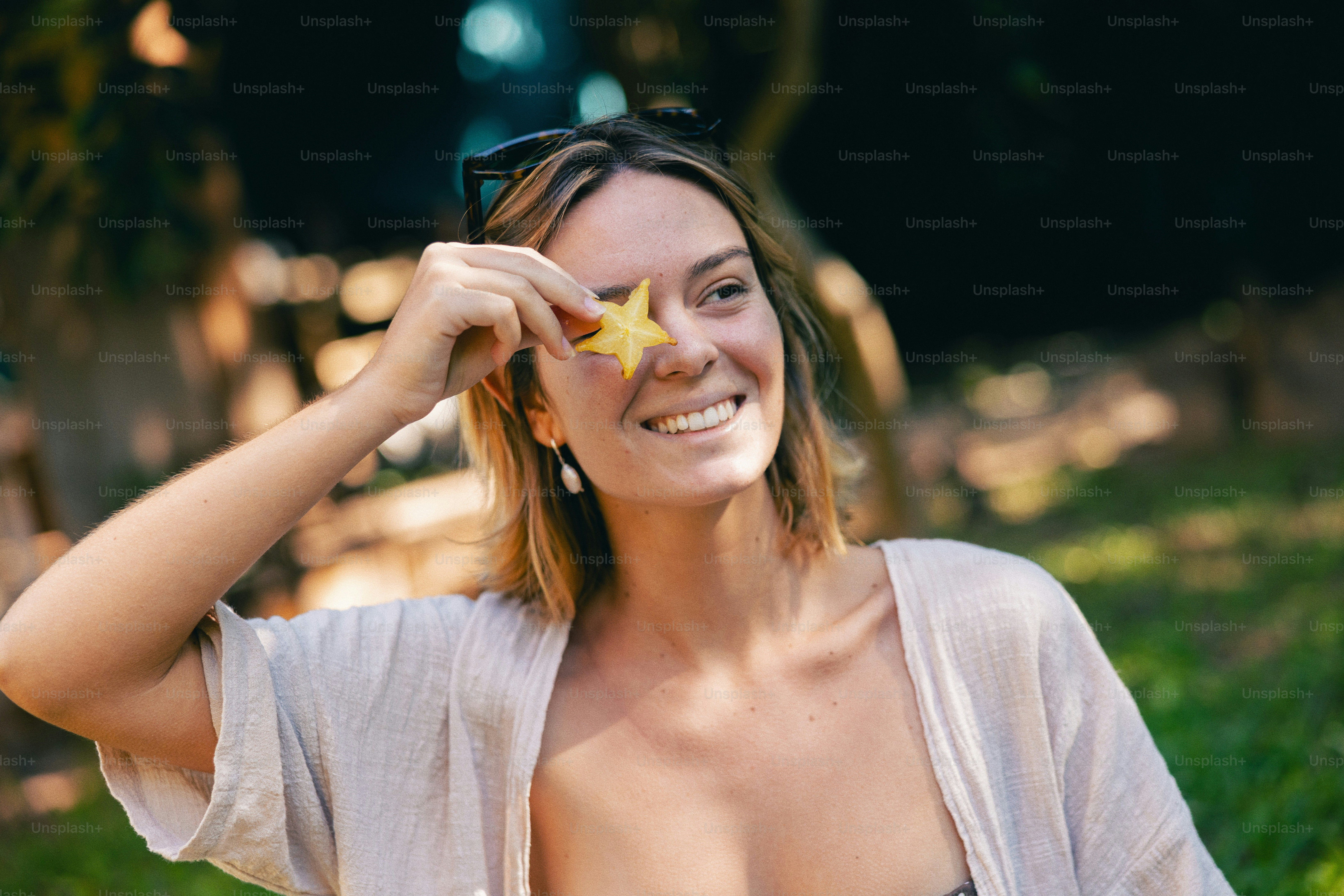 Wanita yang tersenyum memegang irisan belimbing di atas matanya.