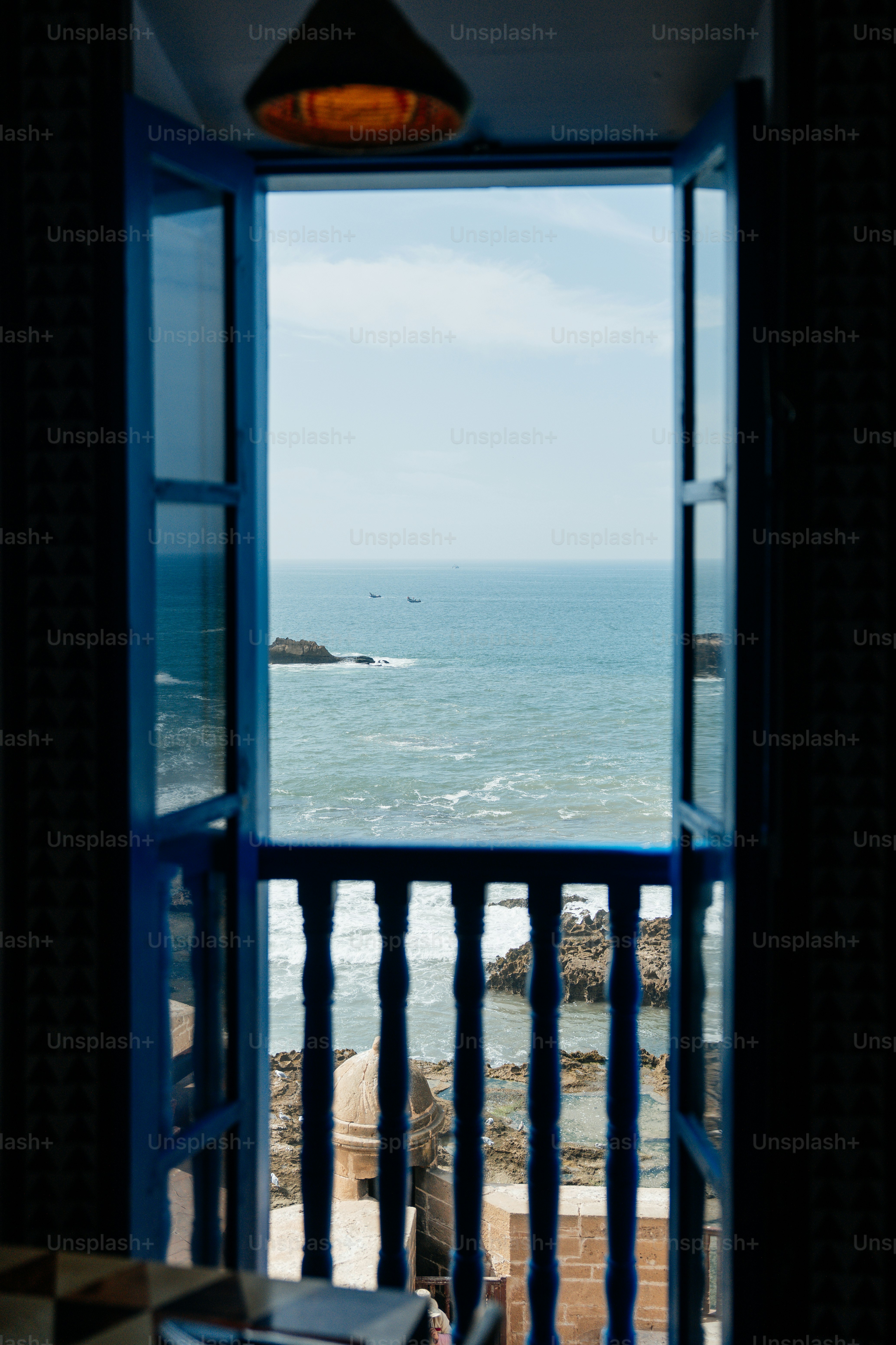 Open blue window overlooking a vast ocean with rocky shore.