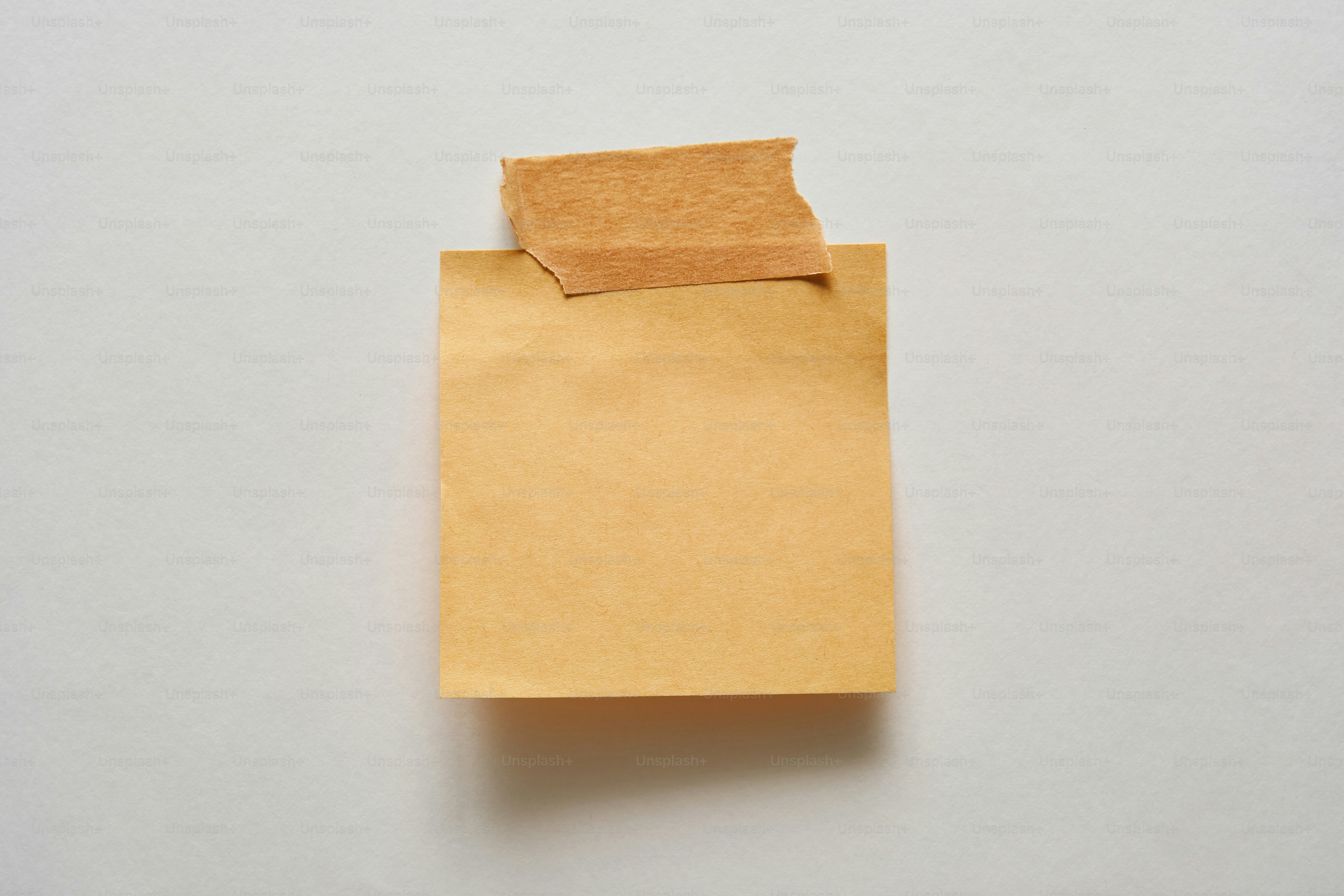 A blank brown sticky note taped to a white background. photo ...