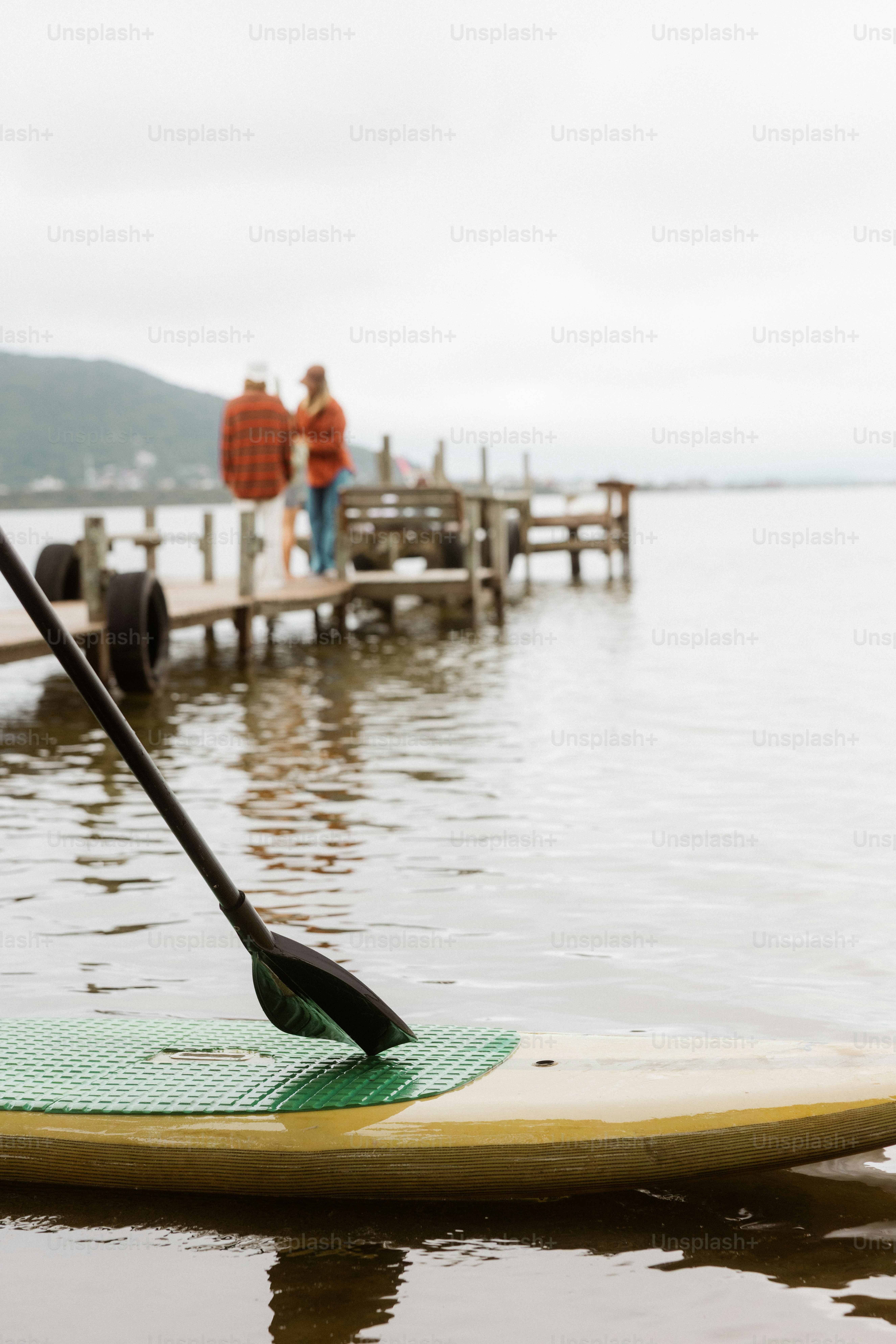 Paddleboard di air dengan orang-orang di dermaga yang jauh.