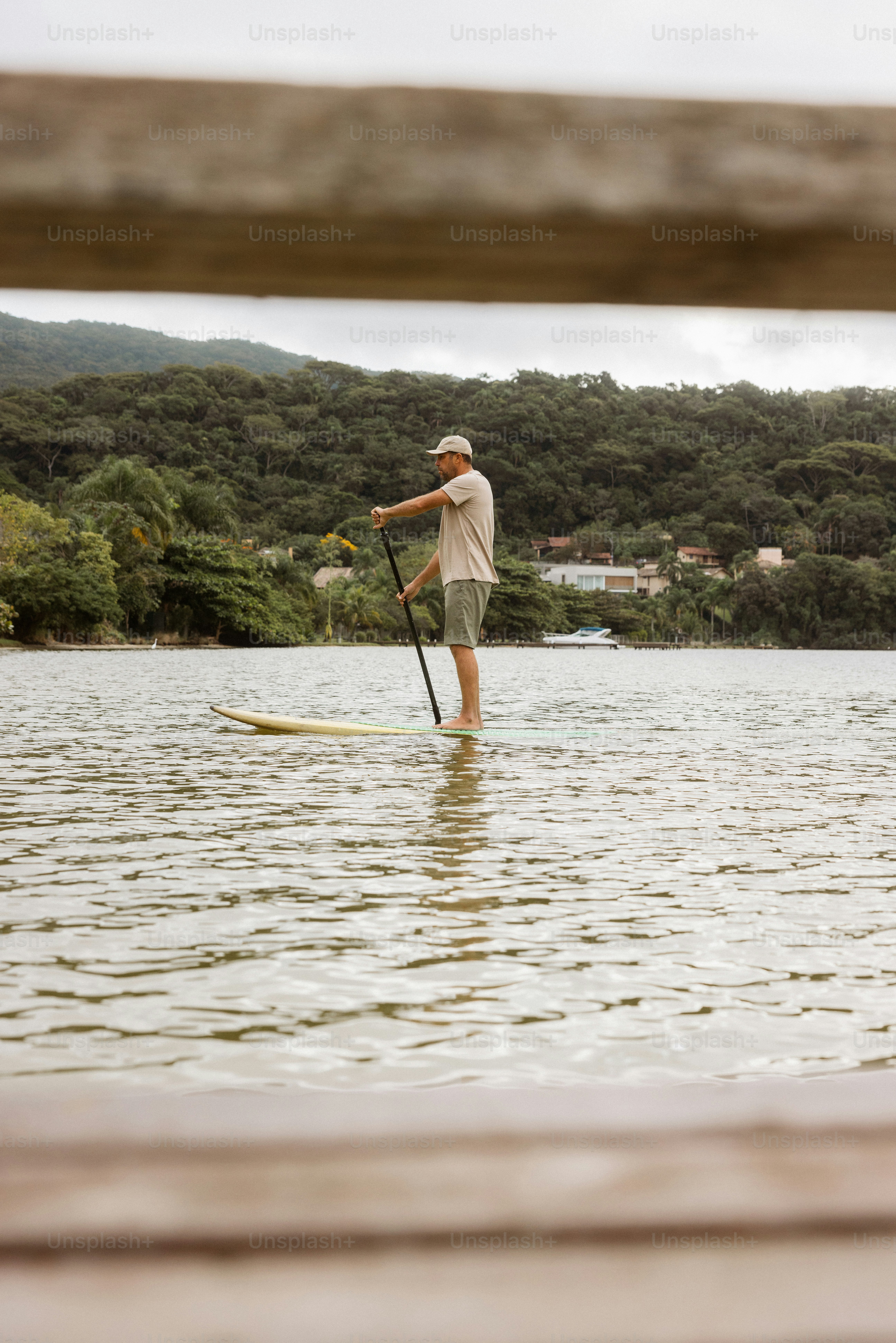 Seorang pria berstand paddleboarding di danau dengan perbukitan hijau.