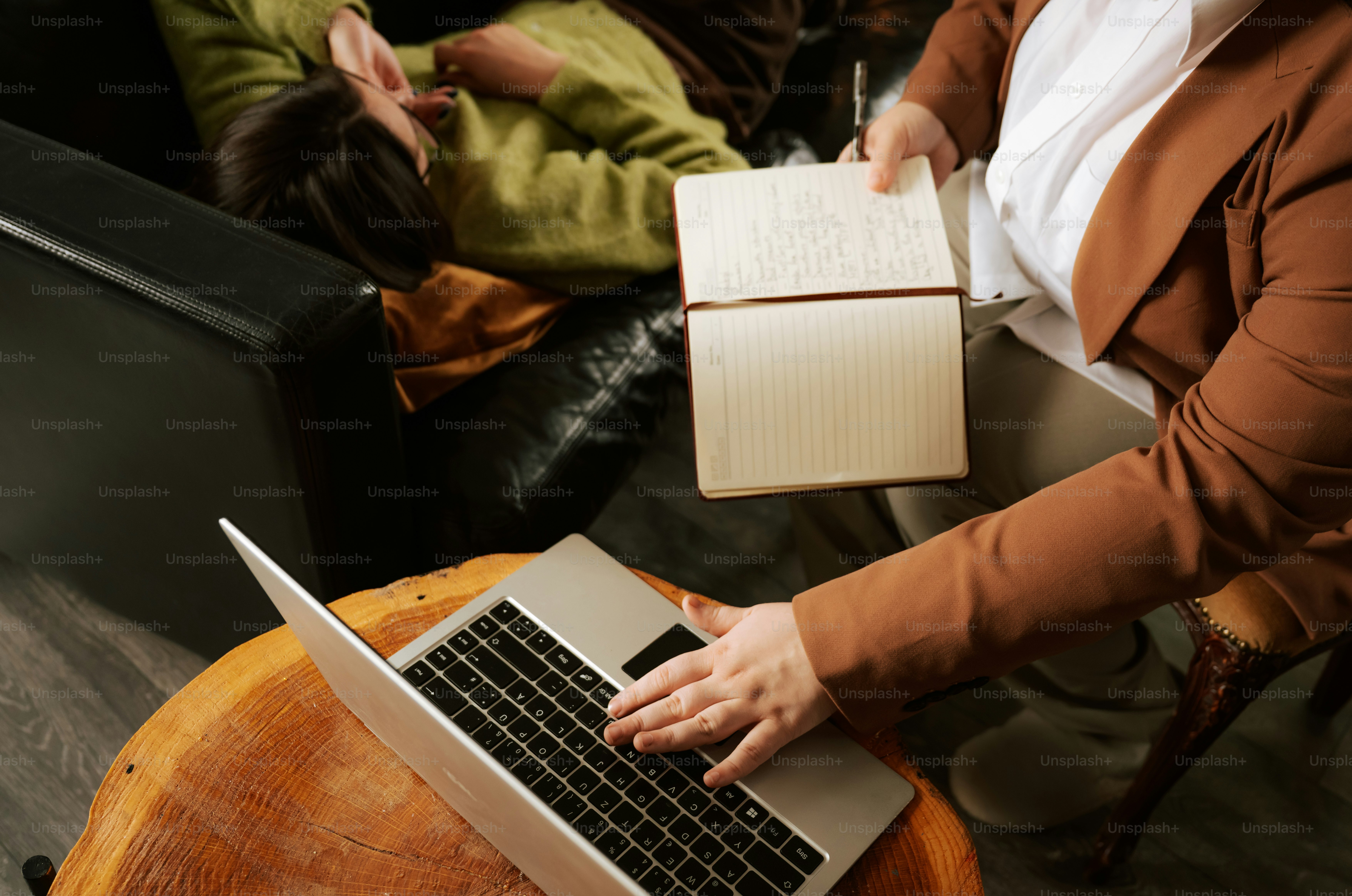 Woman typing on laptop and holding a book indoors.