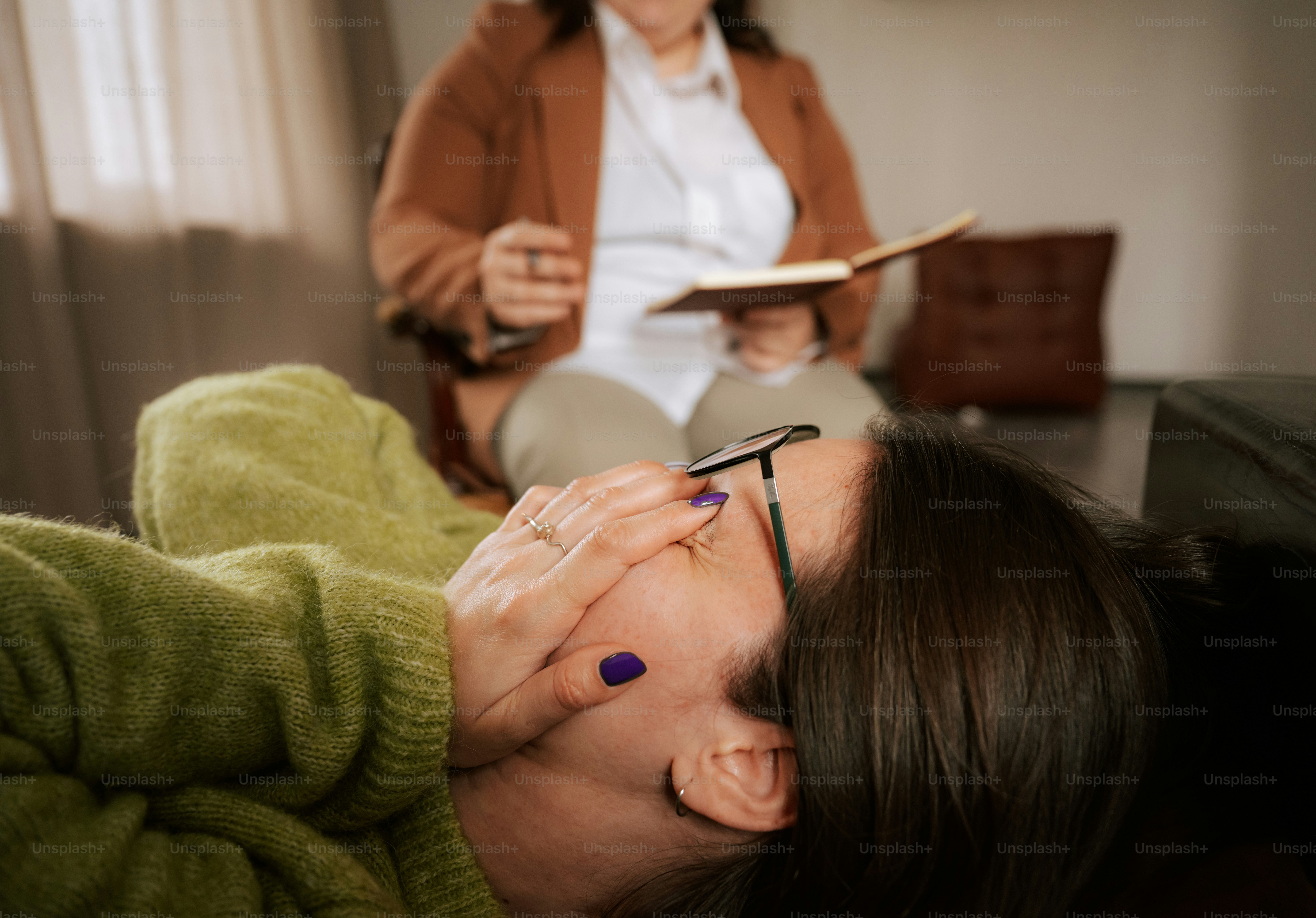 Woman lying on couch covering face during therapy.