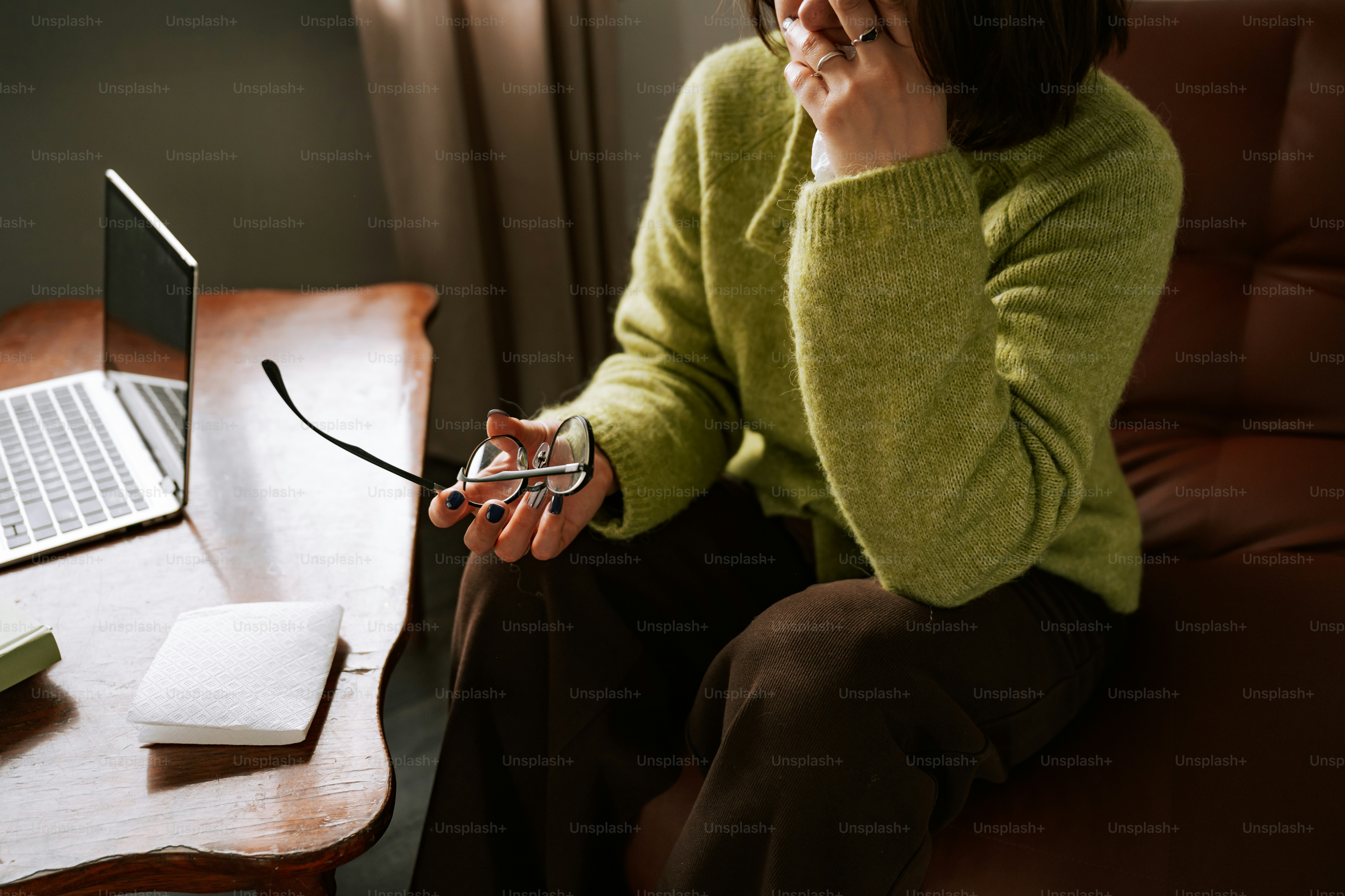 Woman feeling overwhelmed, holding glasses near a laptop.