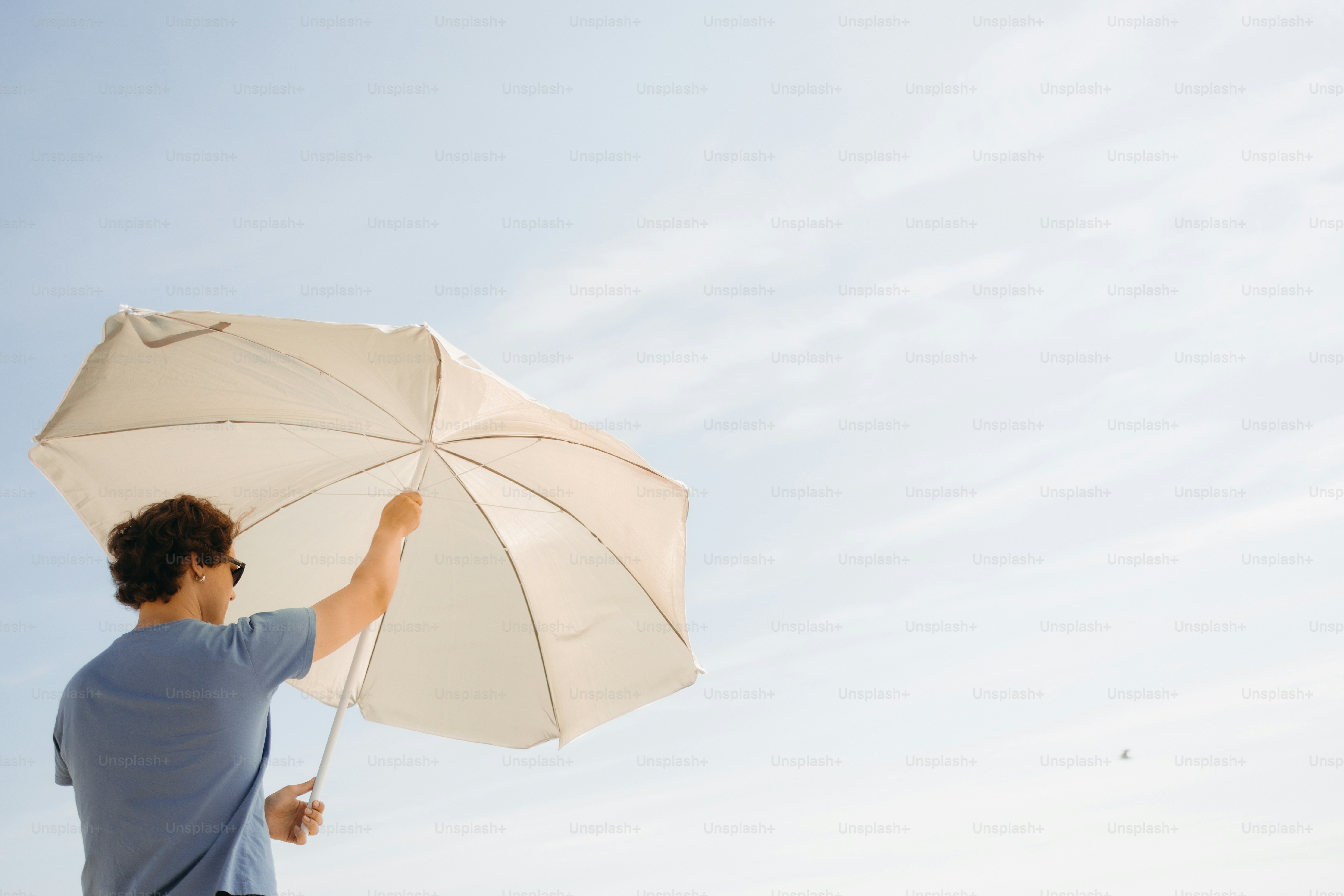 Person in blue shirt holding white umbrella against clear sky.