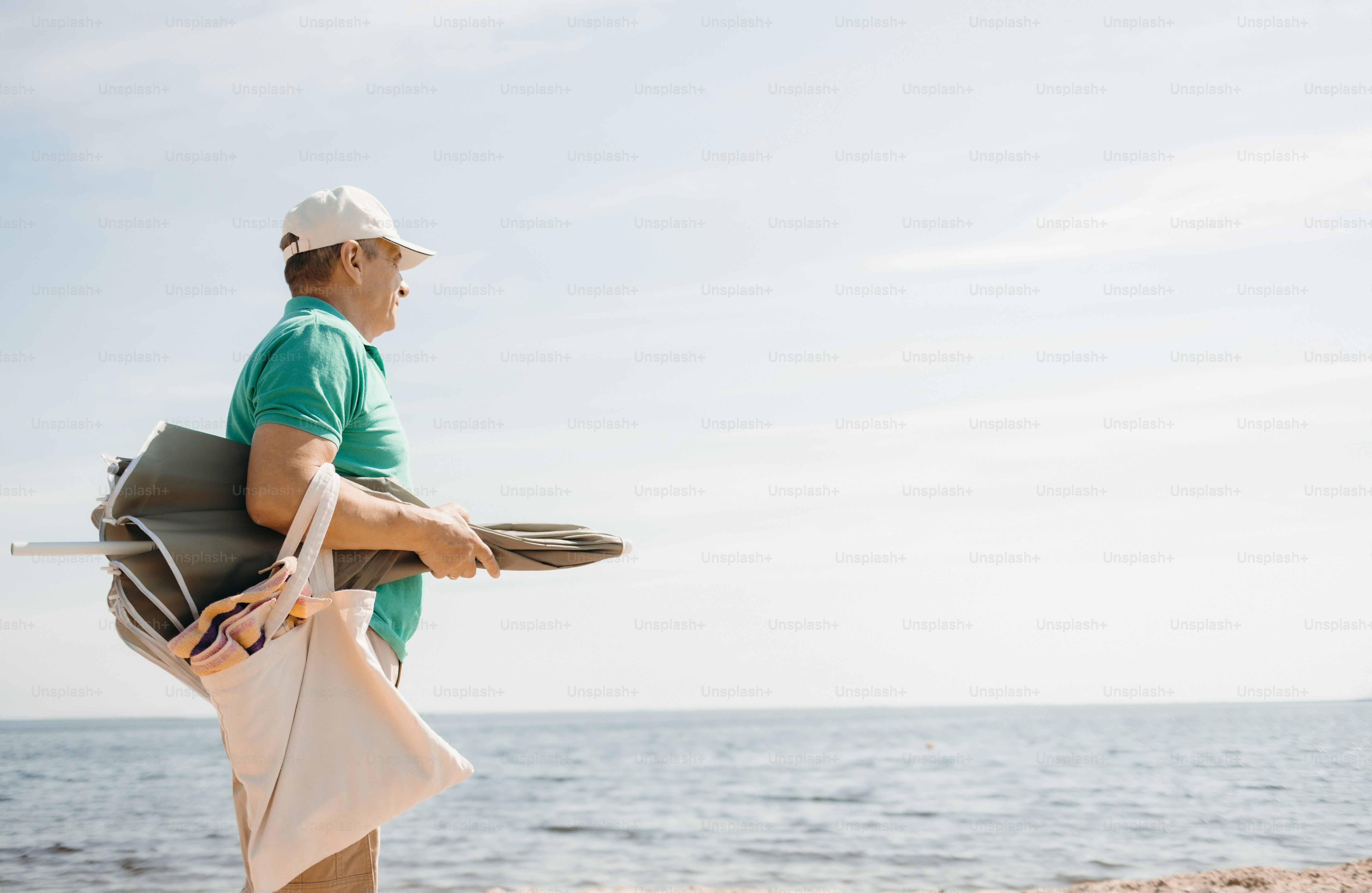 Man walks on beach with folded chair and bag.