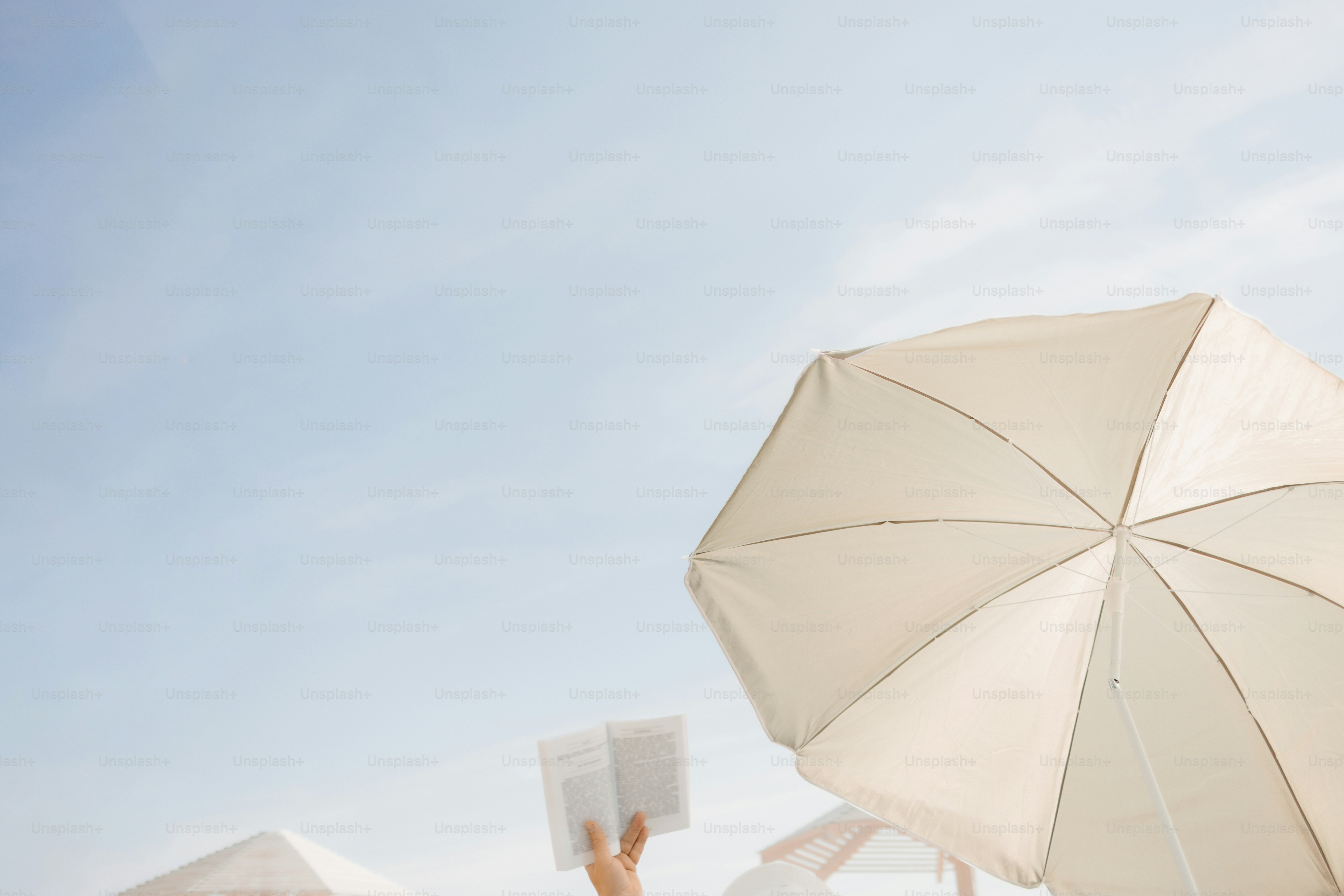 Person reading a book under a white beach umbrella.