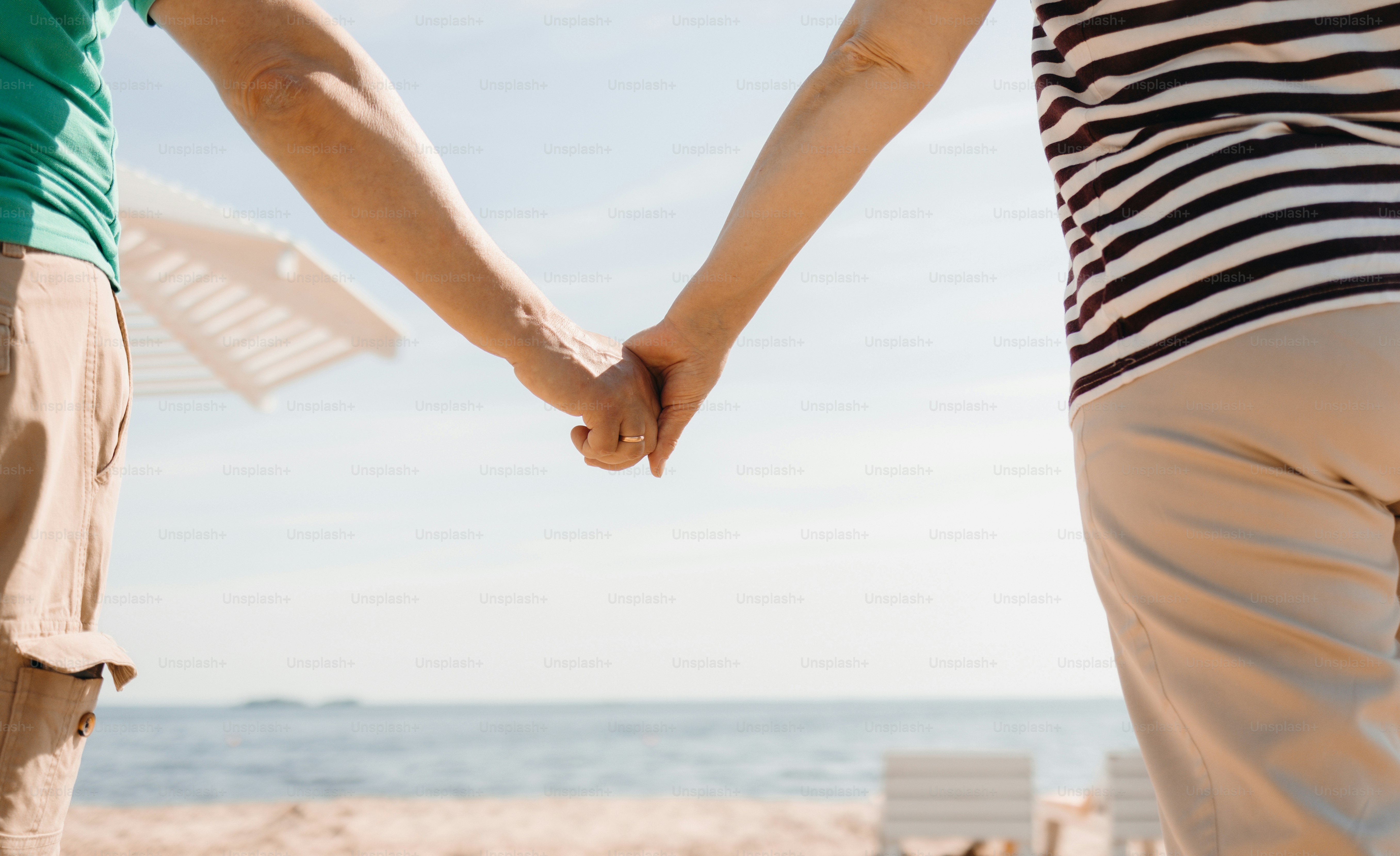 Two people holding hands on a sunny beach.