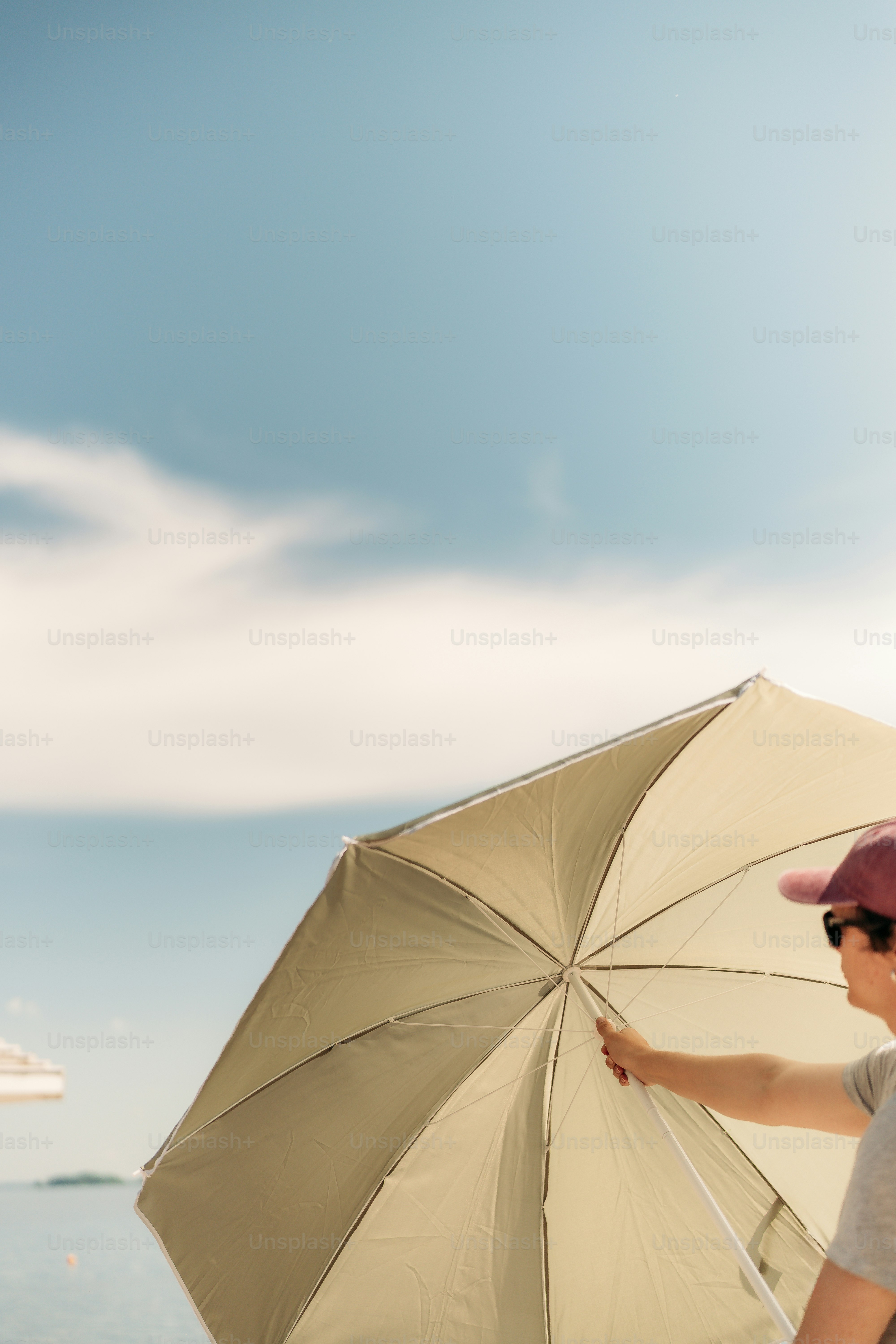 Person holding a beach umbrella under a sunny sky.
