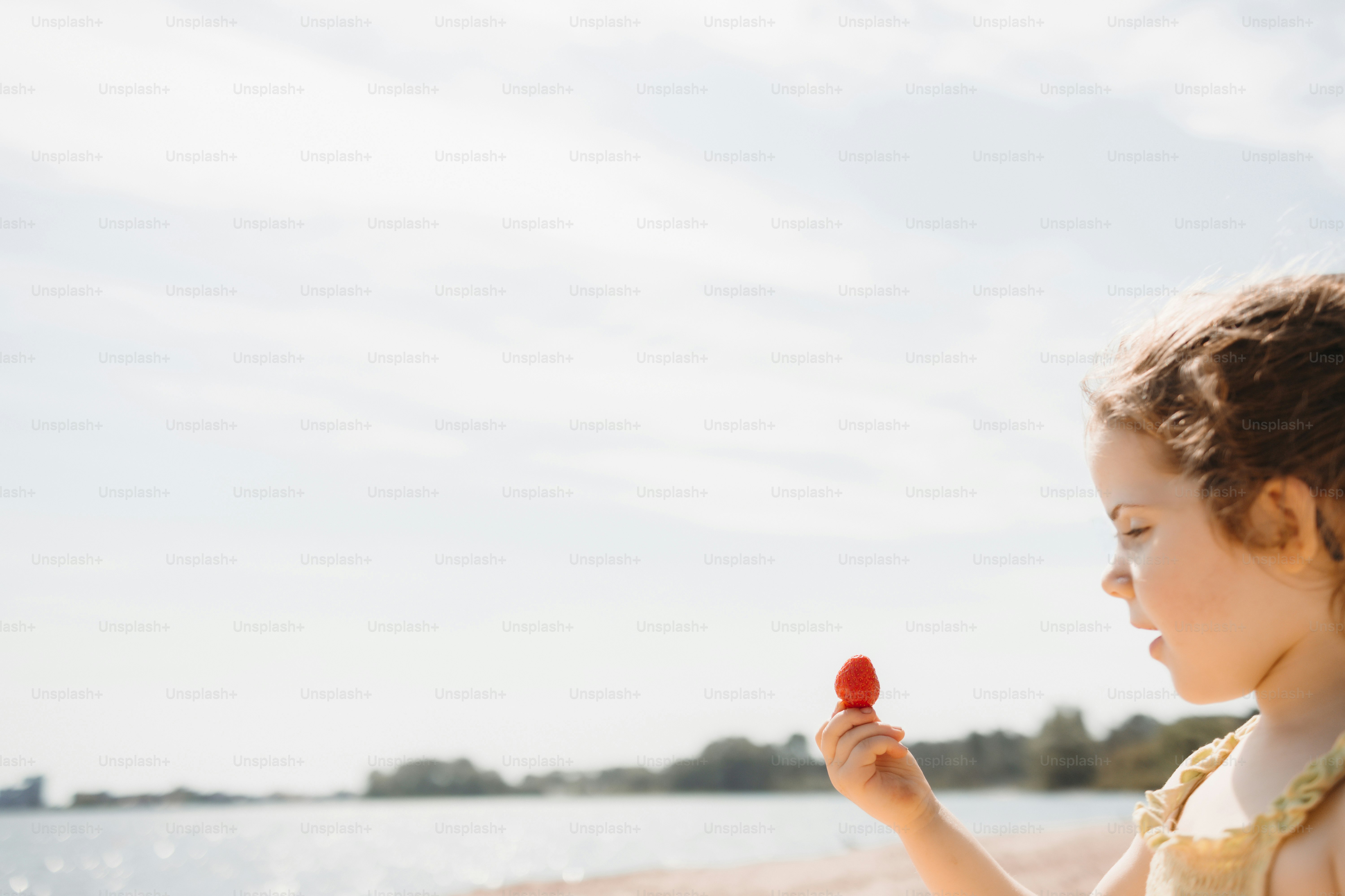 Little girl holding a red object on a sunny beach.