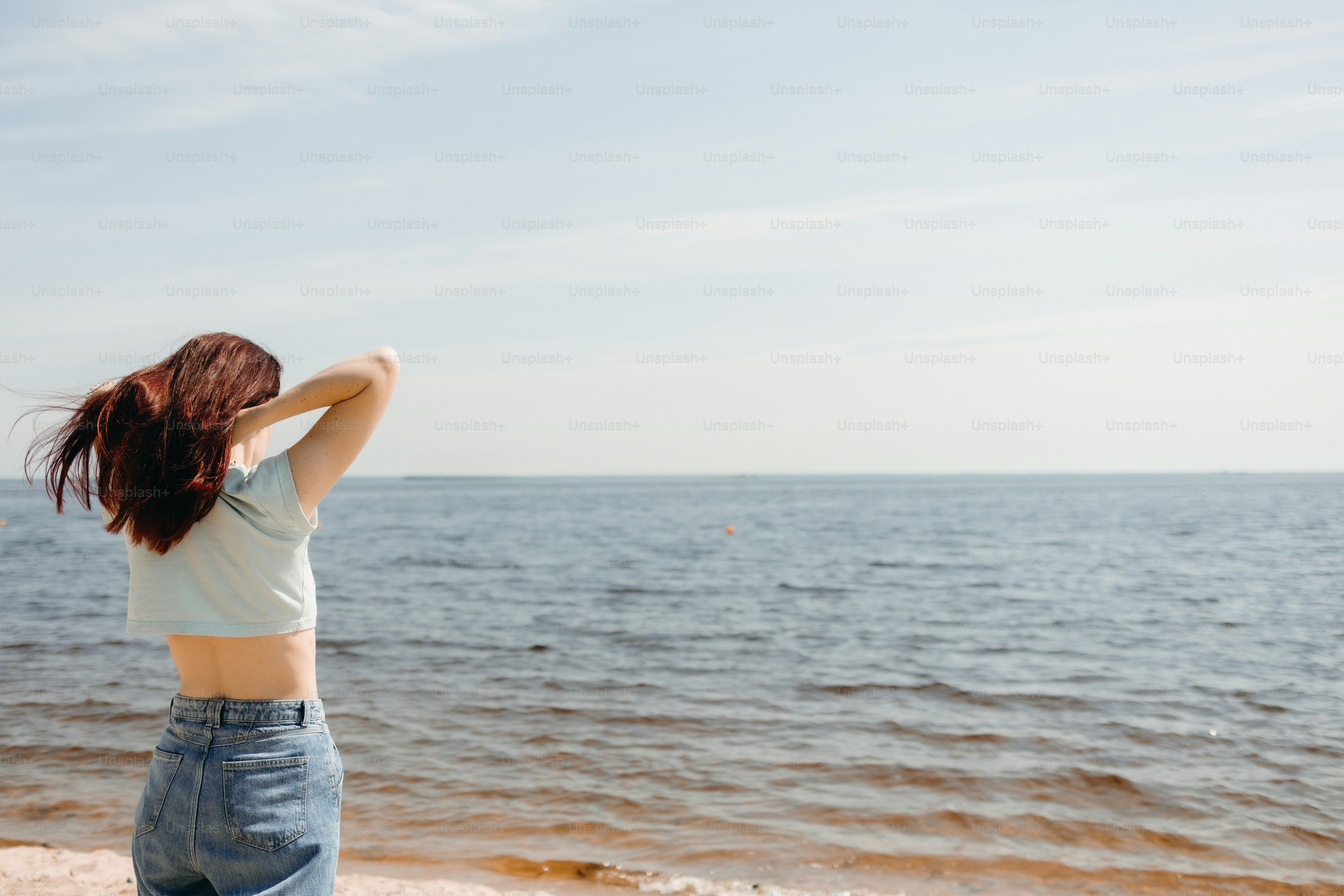 Young woman adjusting her hair while standing by the ocean.