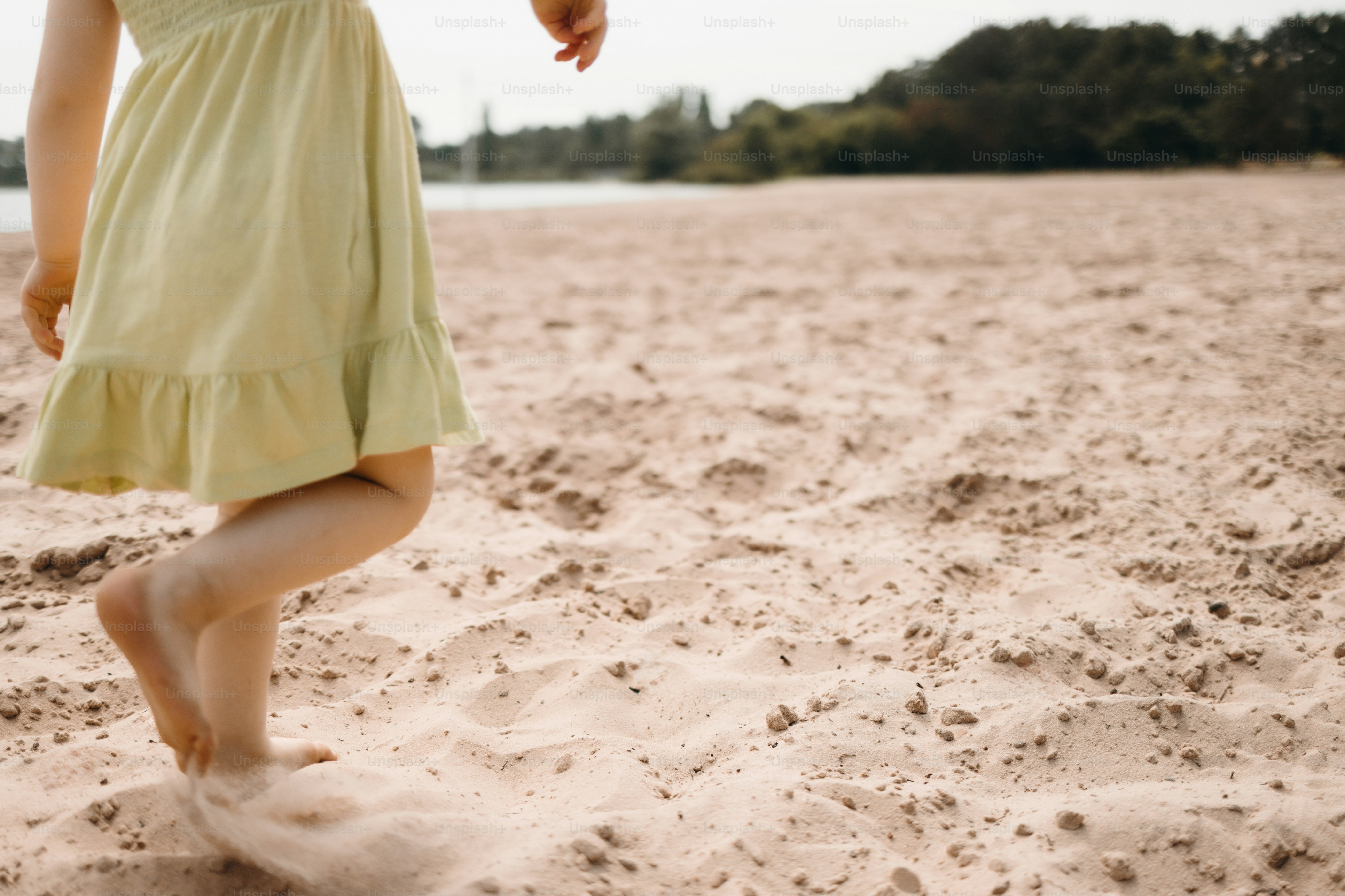 Barefoot child in green dress walking on sandy beach.