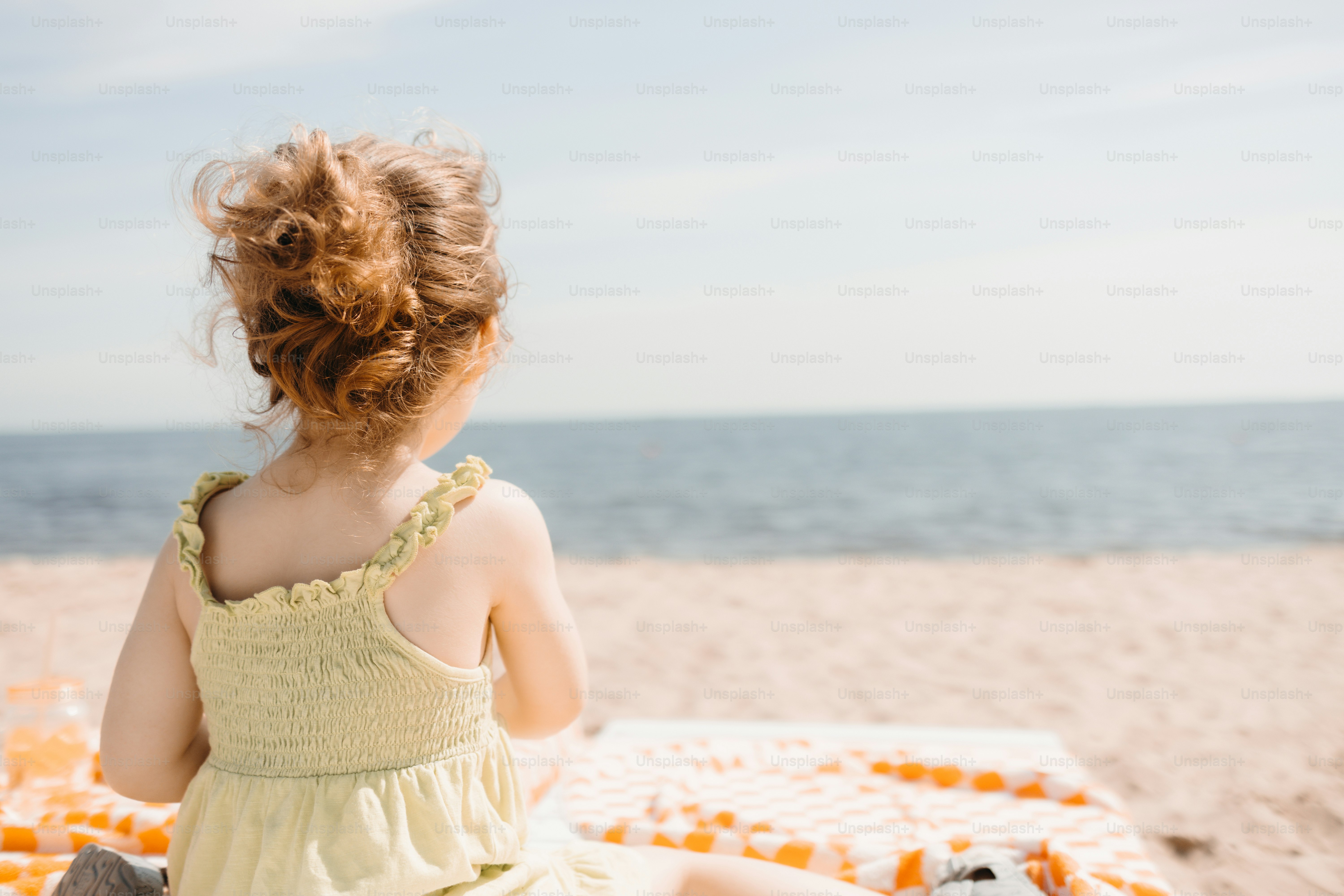 Little girl looking at the ocean from a sandy beach.