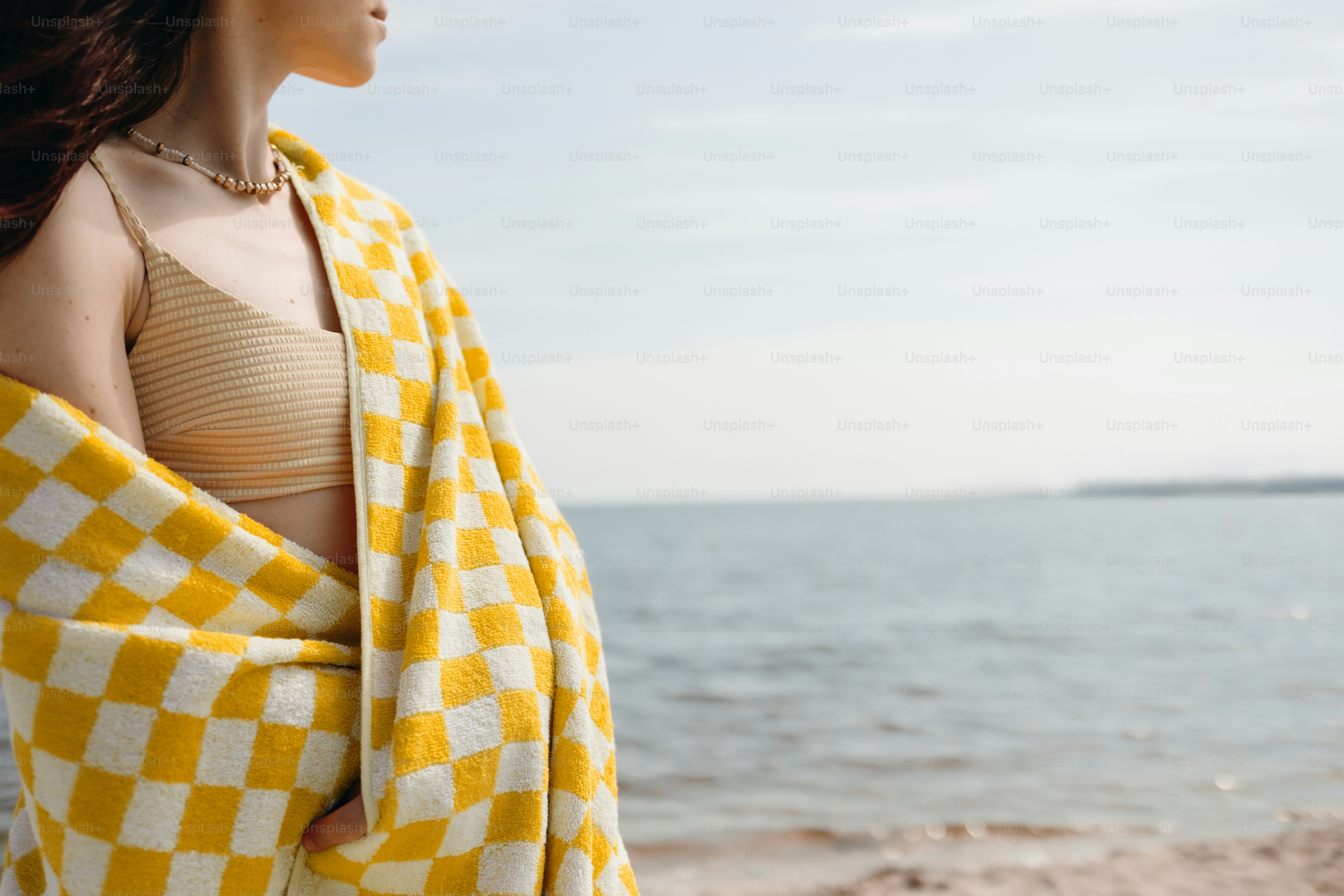 Woman wrapped in a checkered towel looking at the ocean.