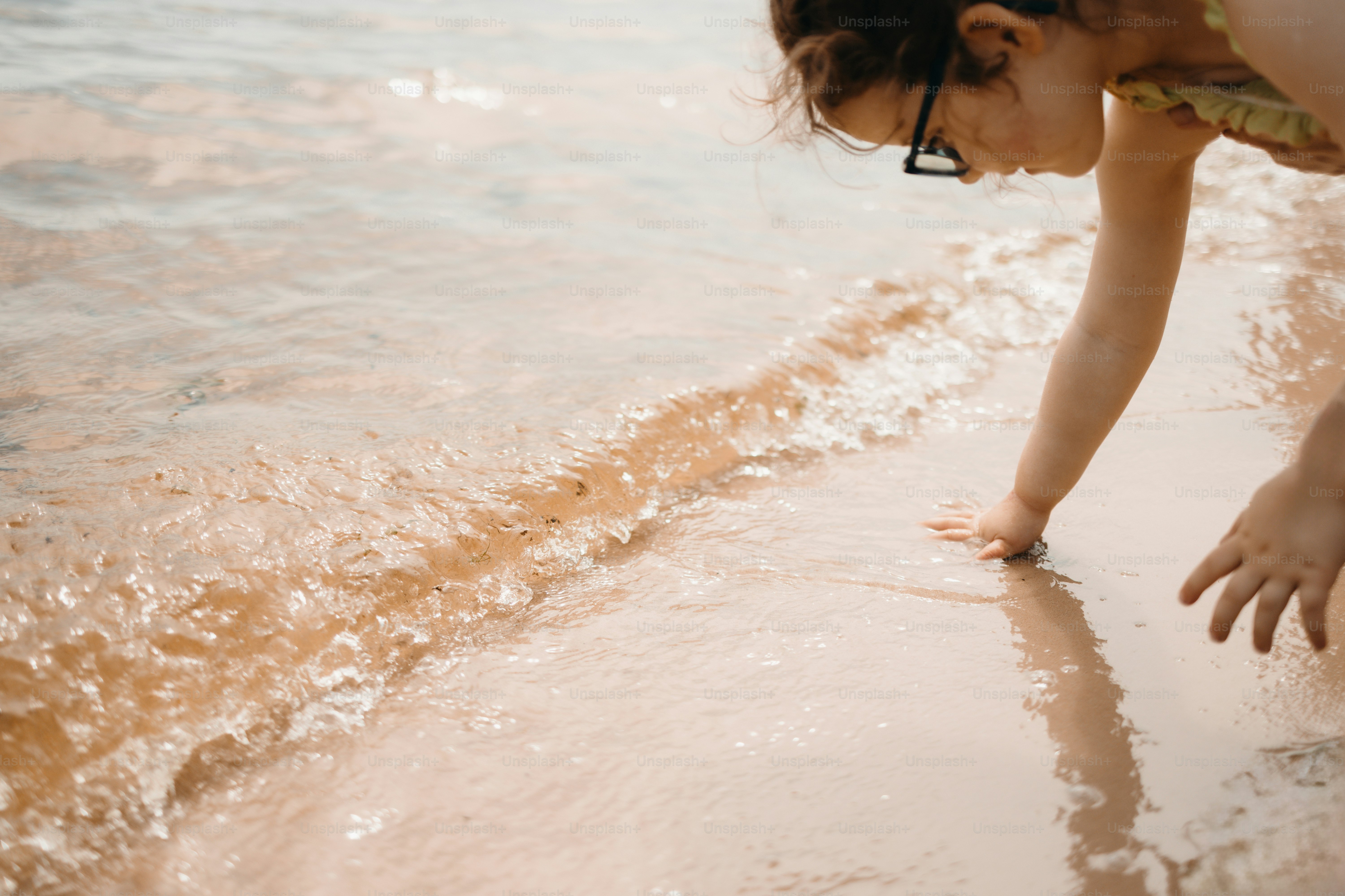 A child plays with water at the sandy shore.
