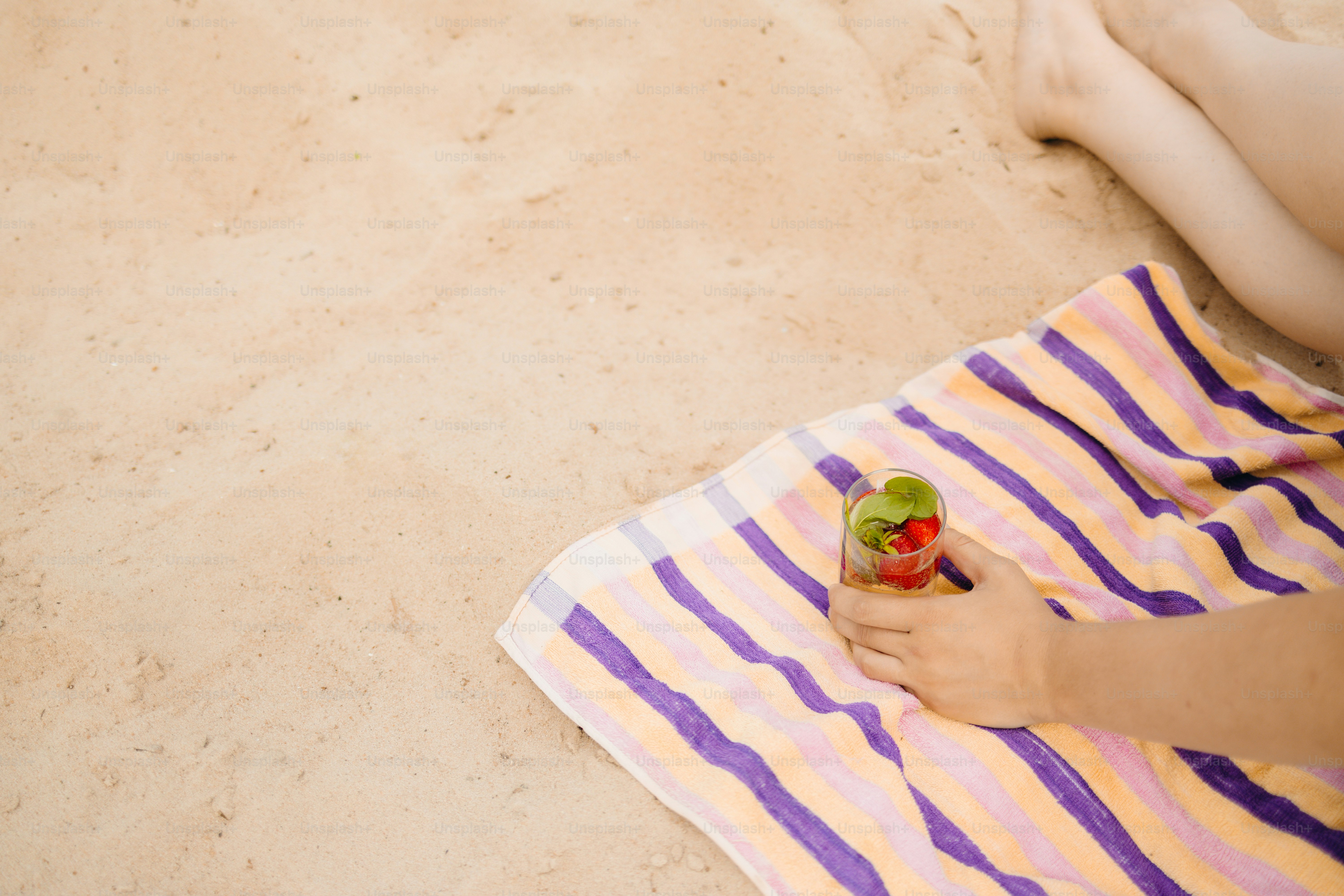 A hand holding a drink on a striped towel.