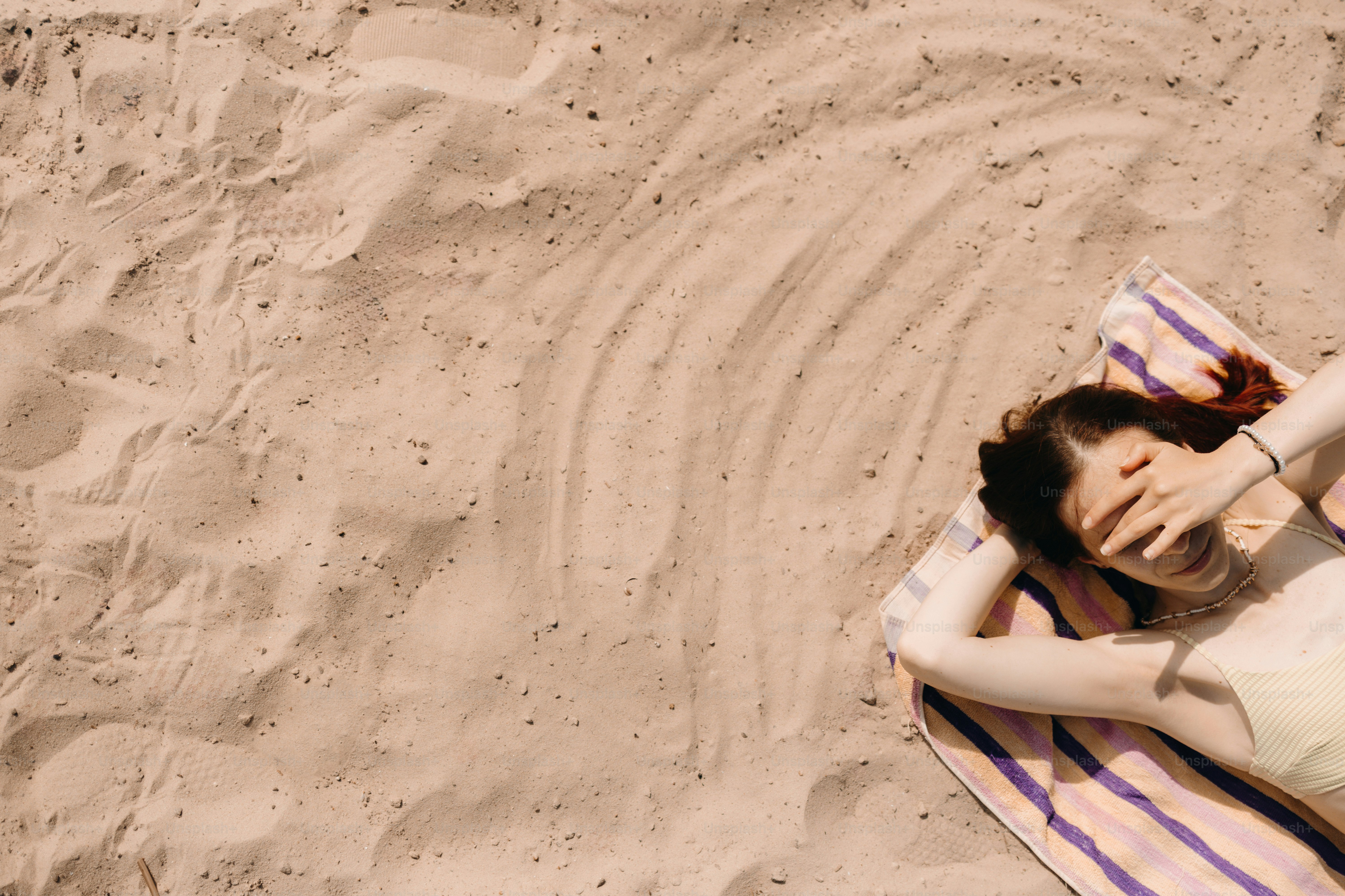Woman relaxing on a striped towel on sandy beach.