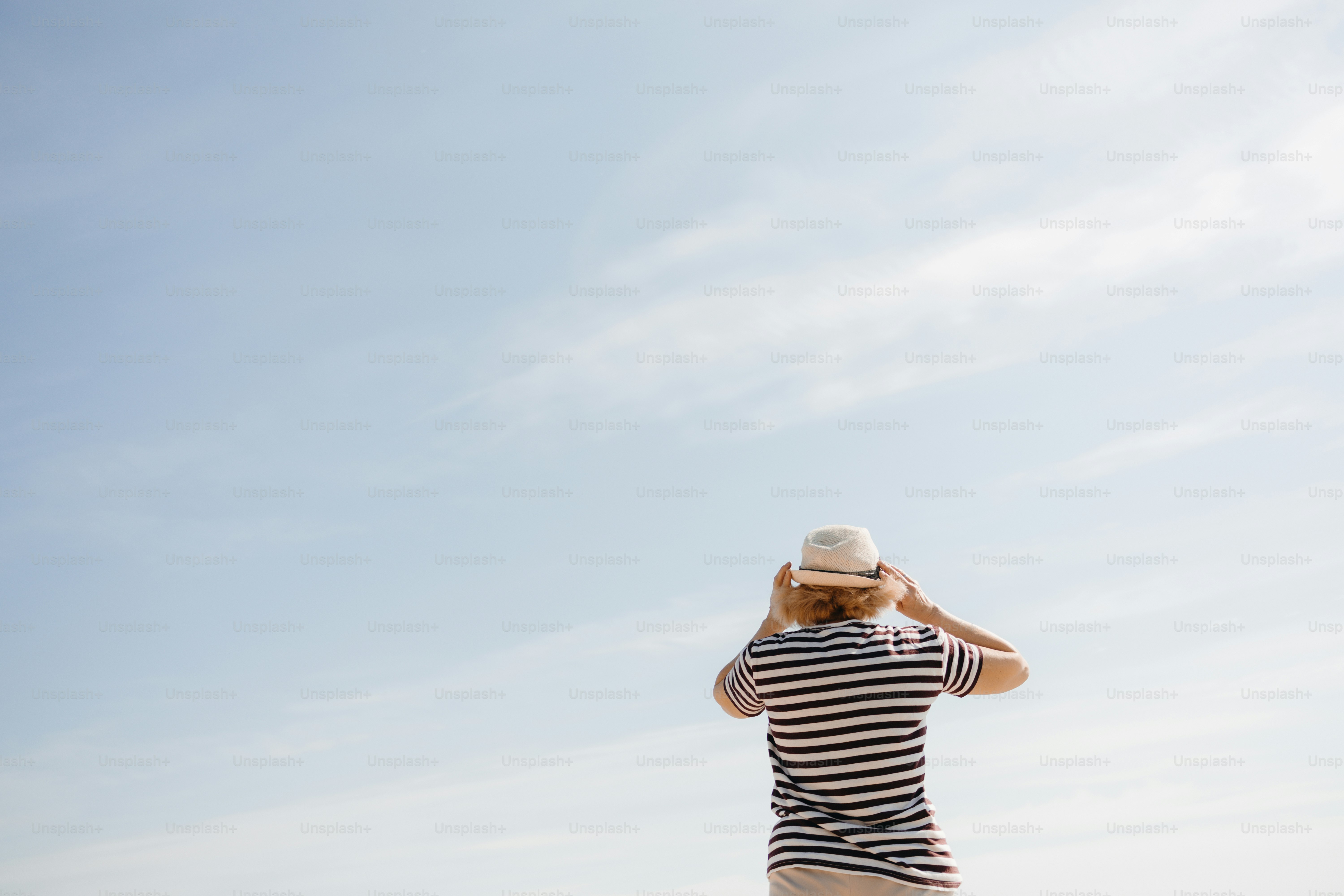 Person in striped shirt and hat looking at blue sky.