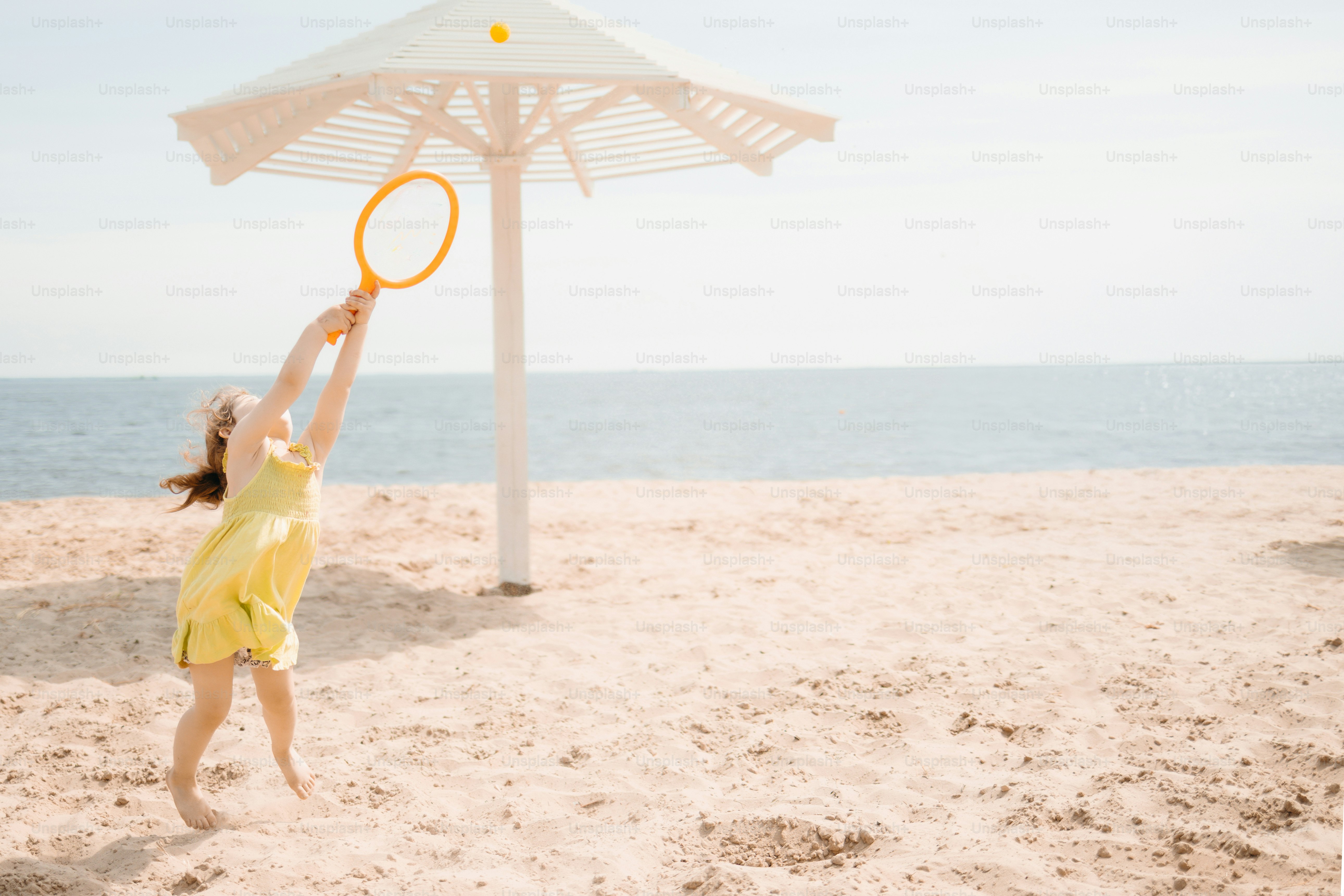 A young girl plays badminton on a sandy beach.