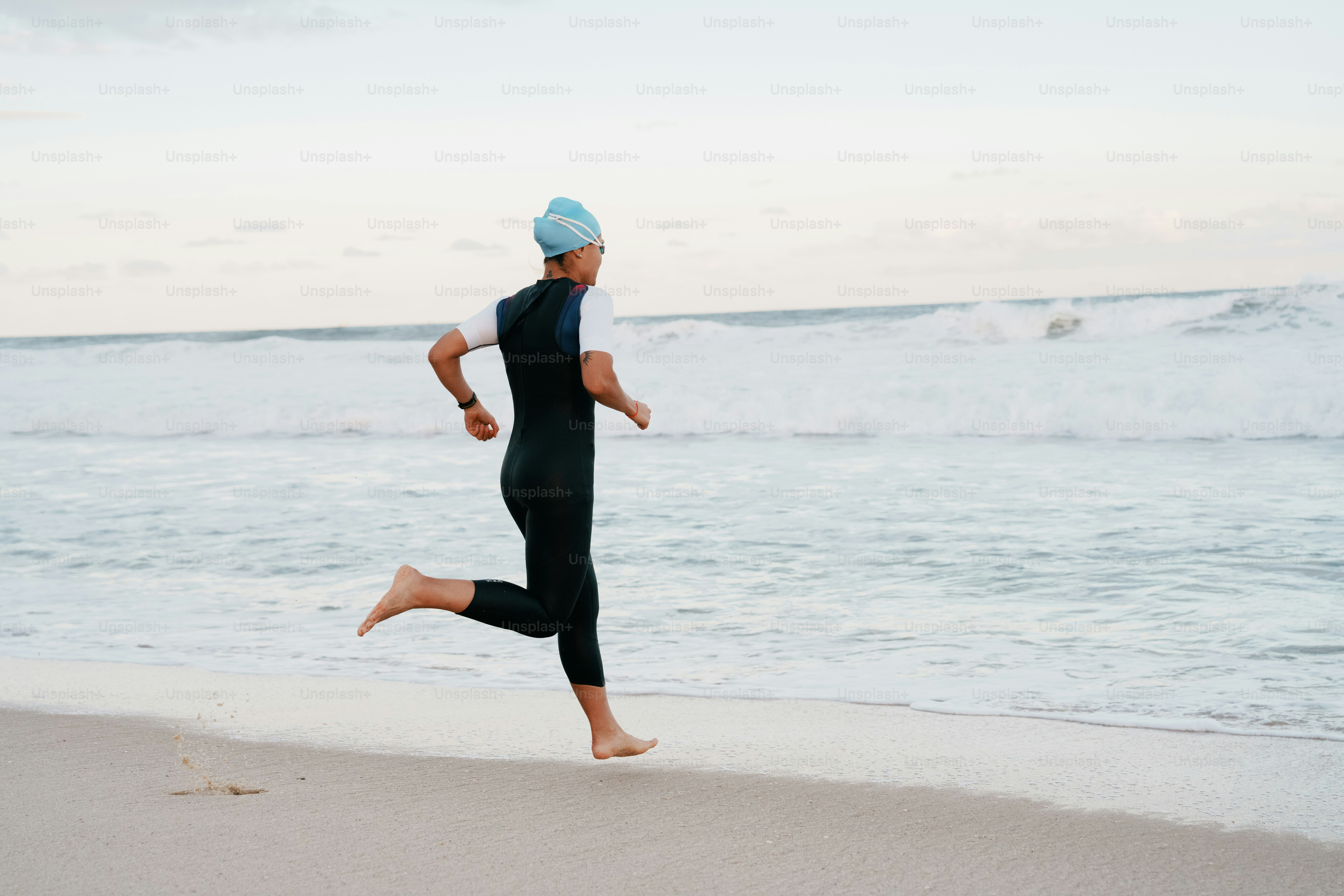 A person in a wetsuit runs barefoot on the beach