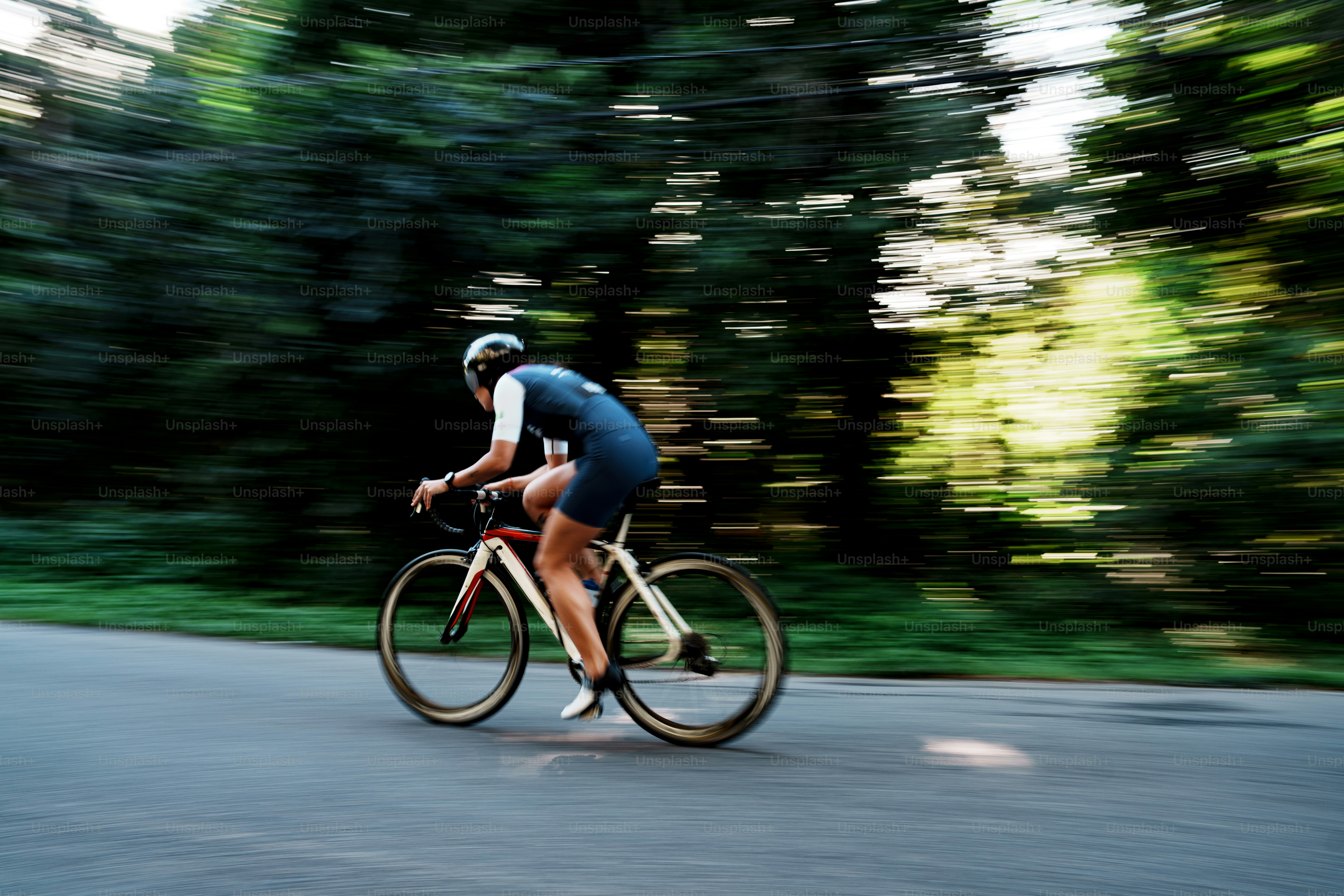 Person cycling fast on a road with blurred green trees