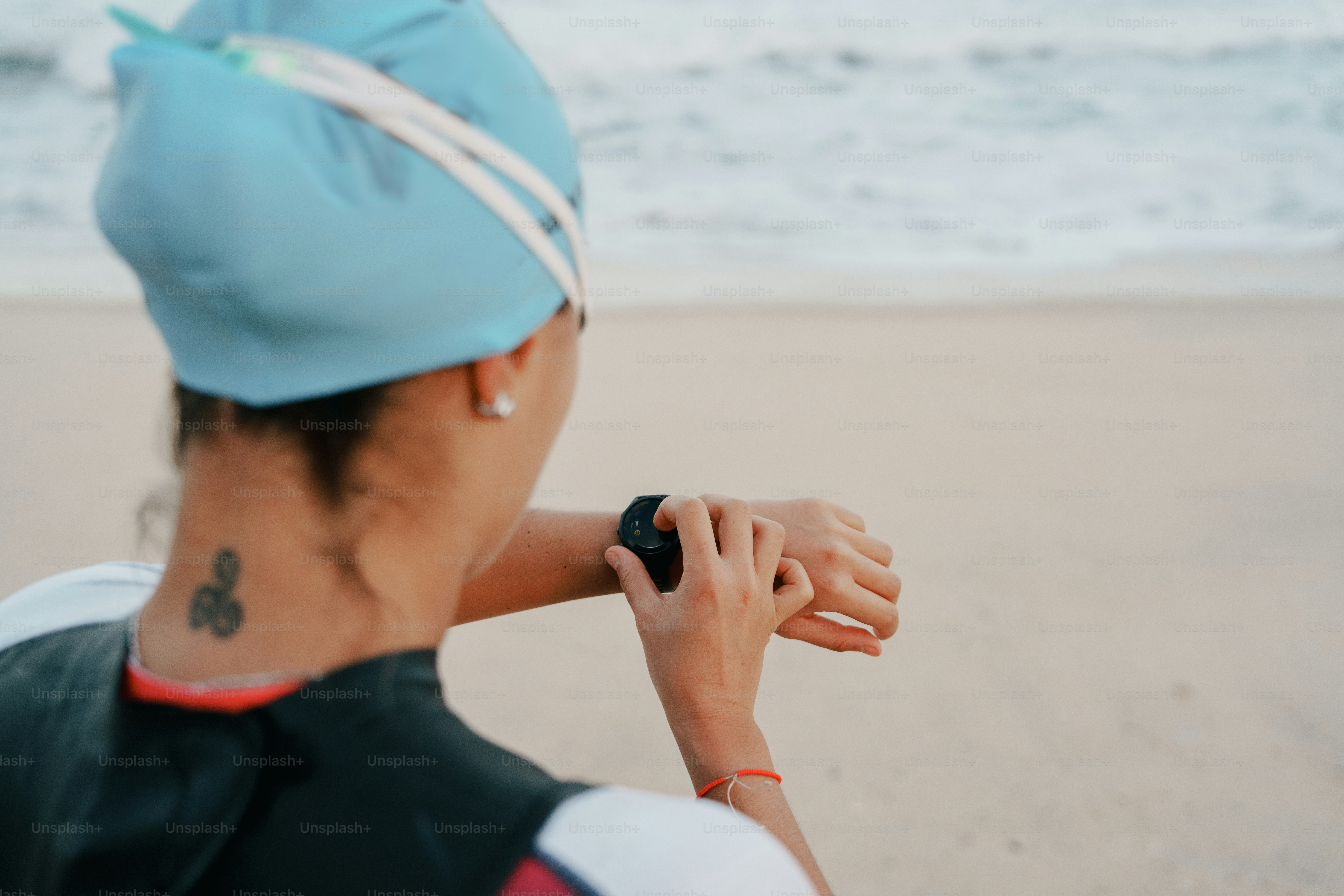 Swimmer in wetsuit and cap checking smartwatch by the ocean.