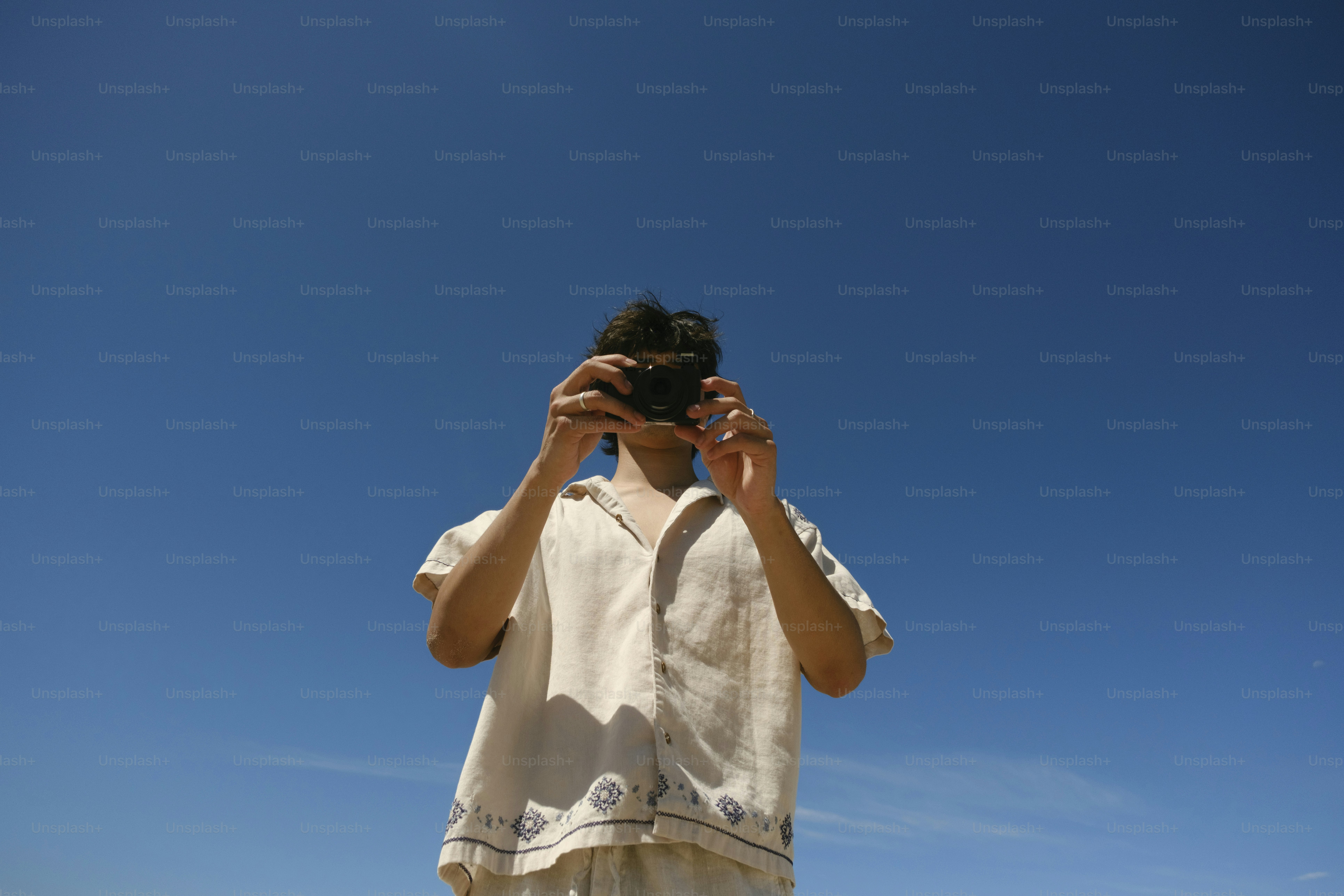 Person holding a camera against a bright blue sky.