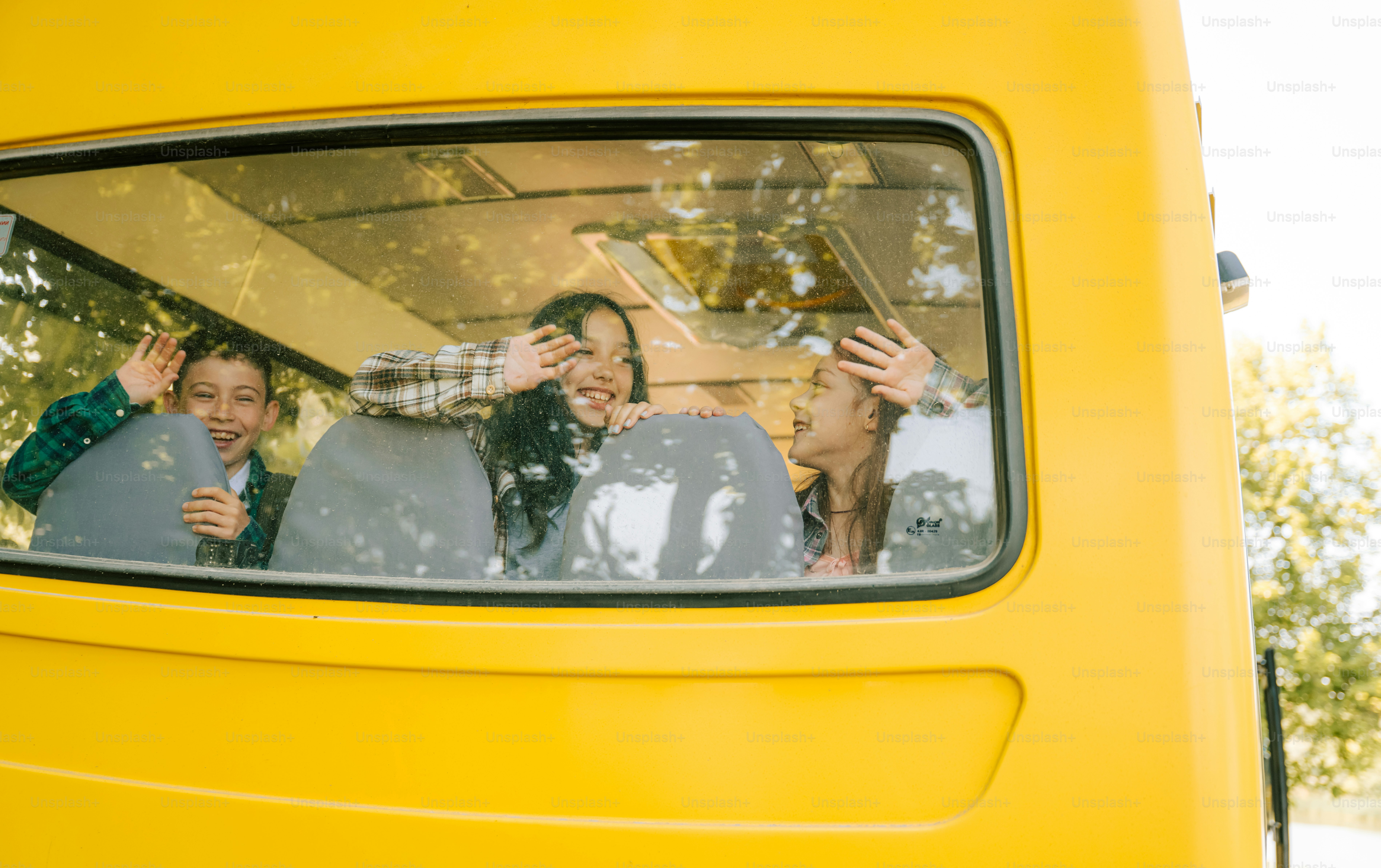 Kids waving happily from a yellow school bus window