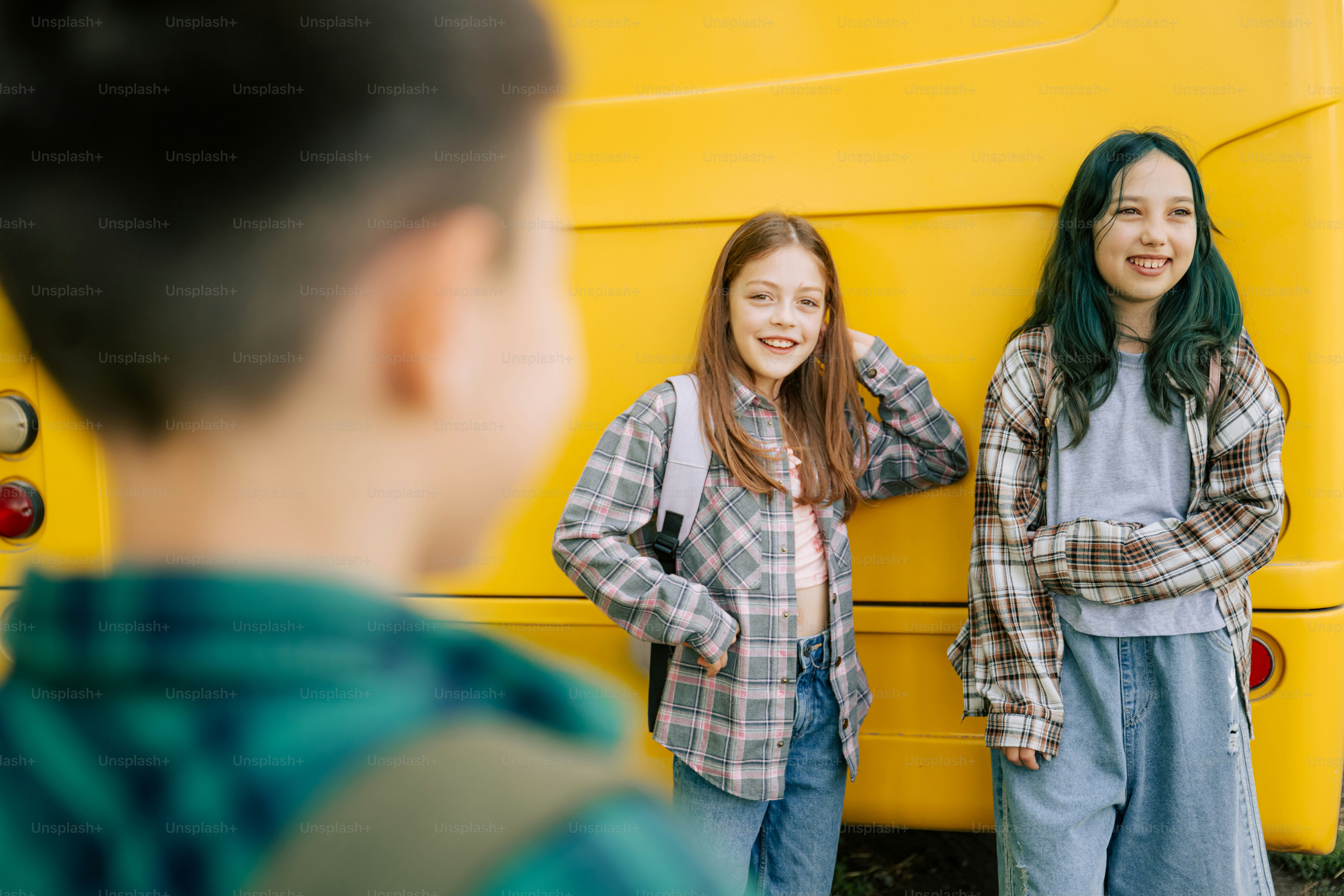 Dos chicas sonrientes están junto a un autobús escolar amarillo