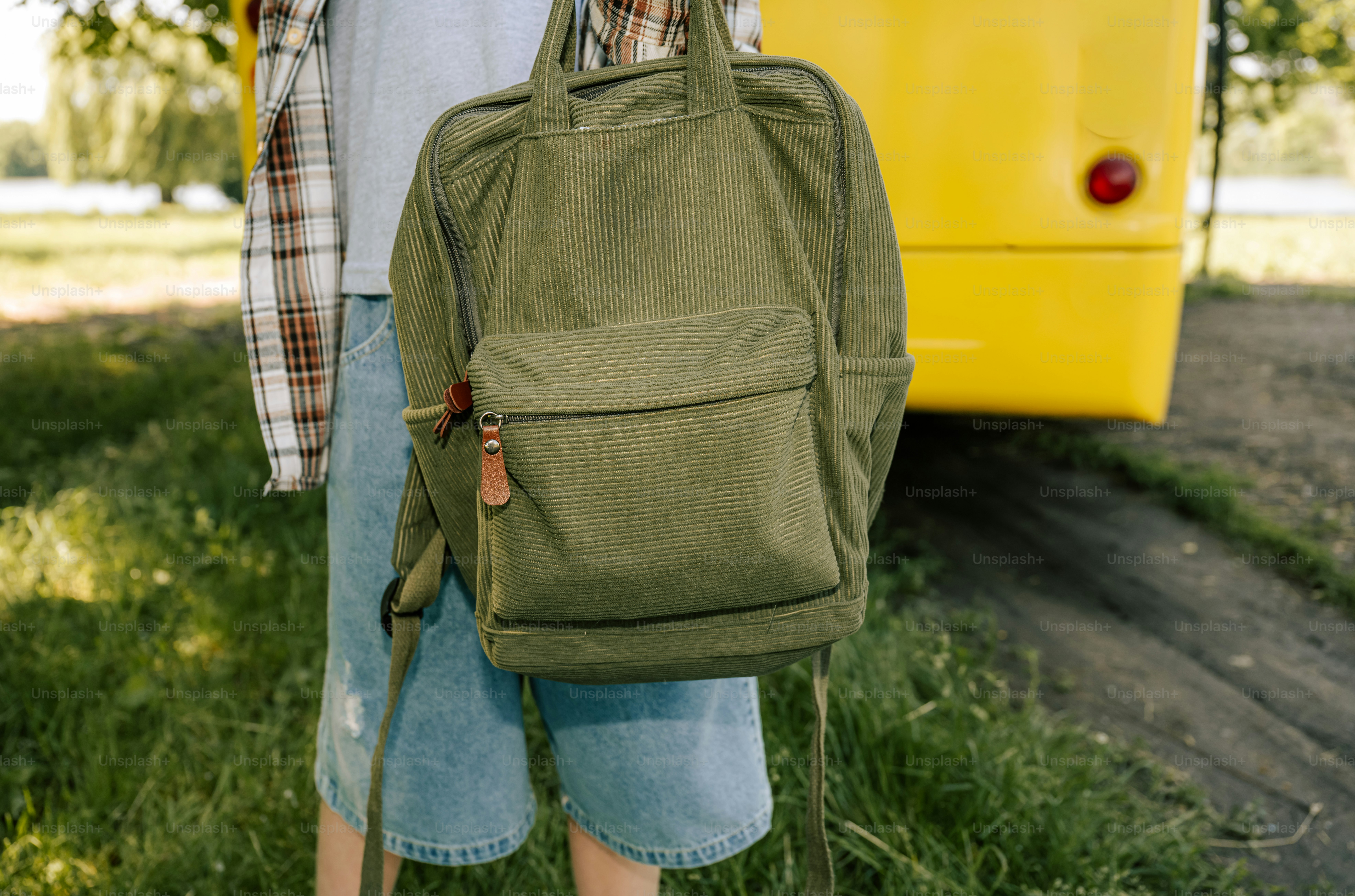 Person with a green backpack standing by a yellow bus