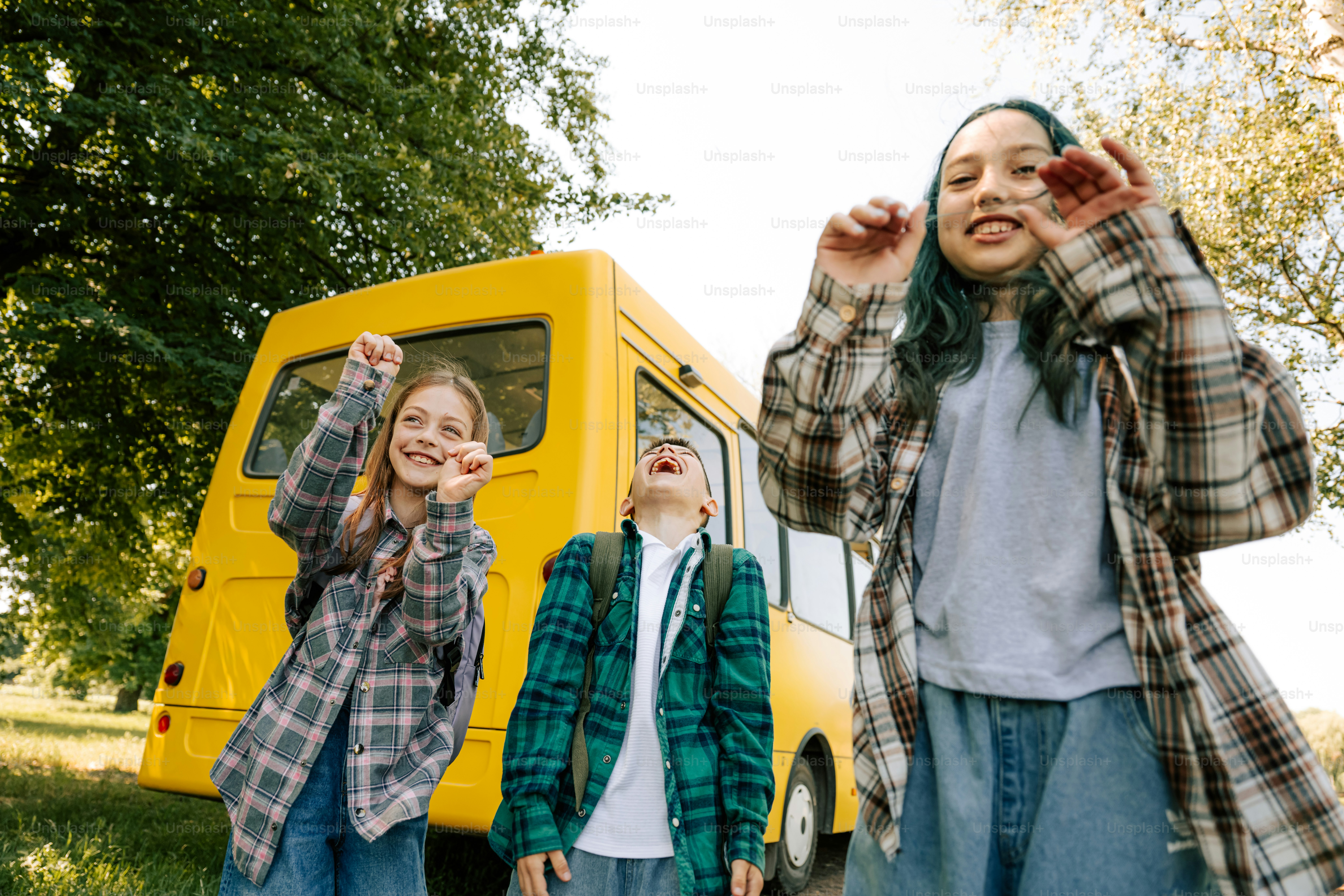 Three cheerful kids in plaid shirts by a yellow bus