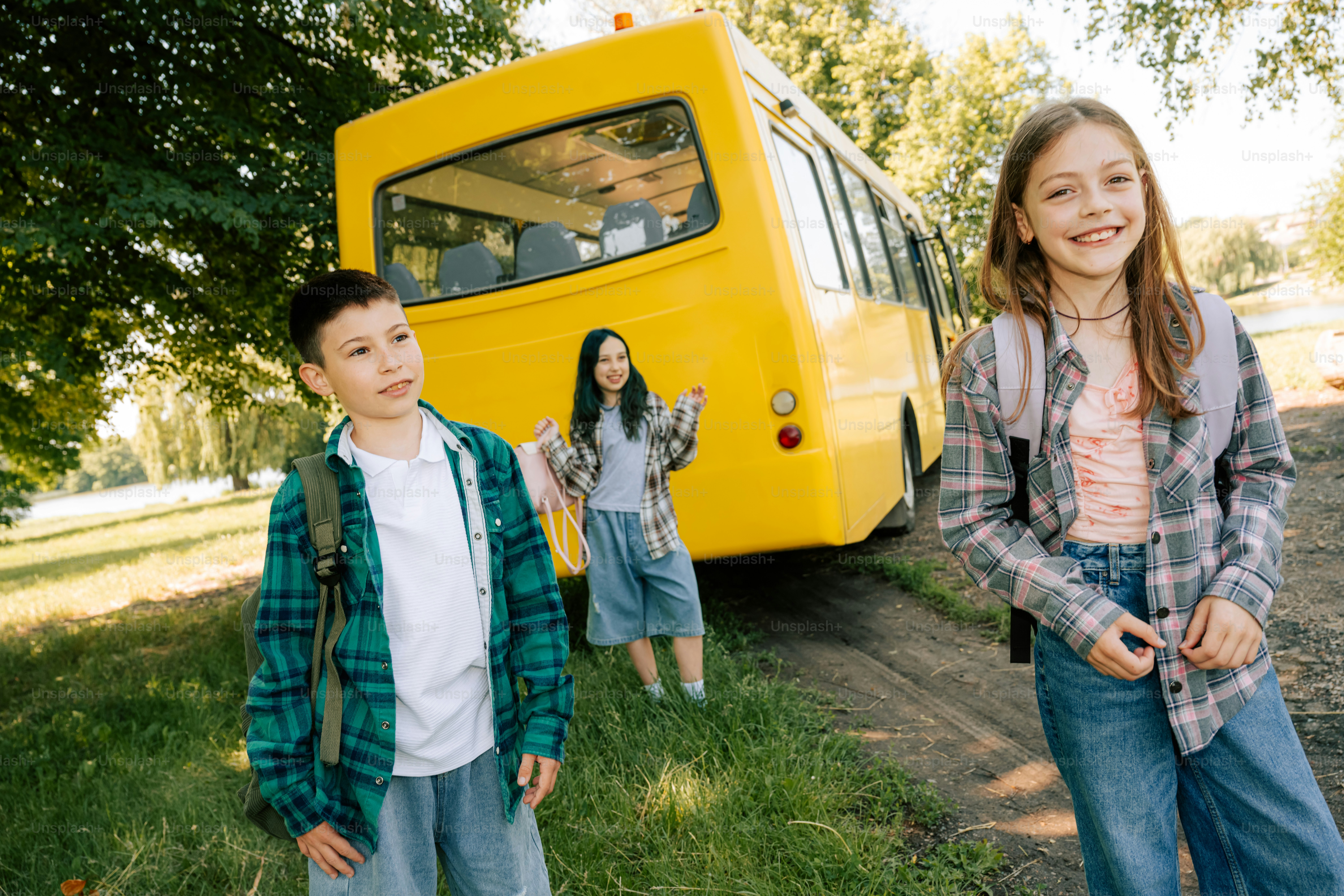 Tiga anak berdiri di dekat bus sekolah kuning di luar ruangan
