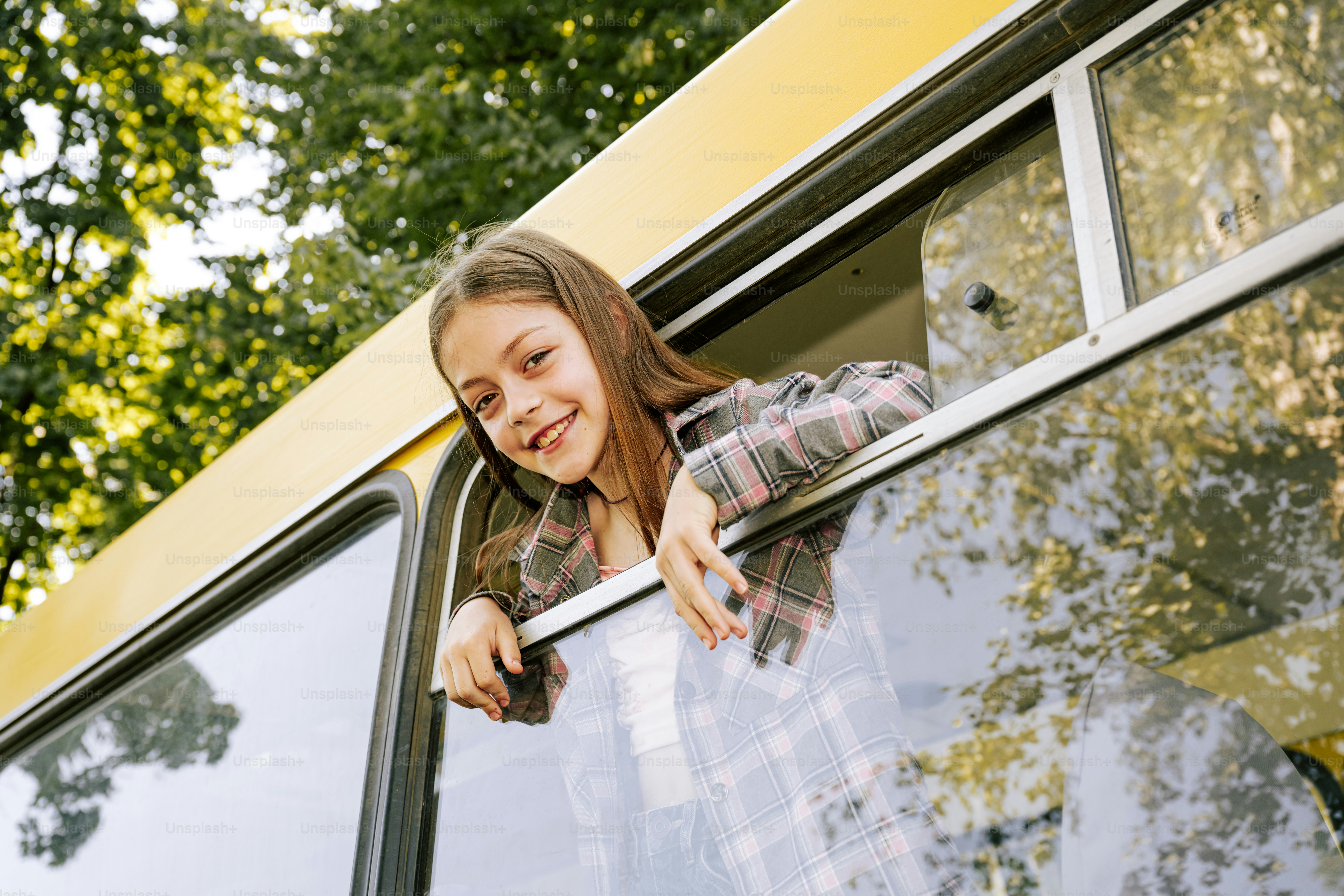 A young girl smiles while looking out a bus window