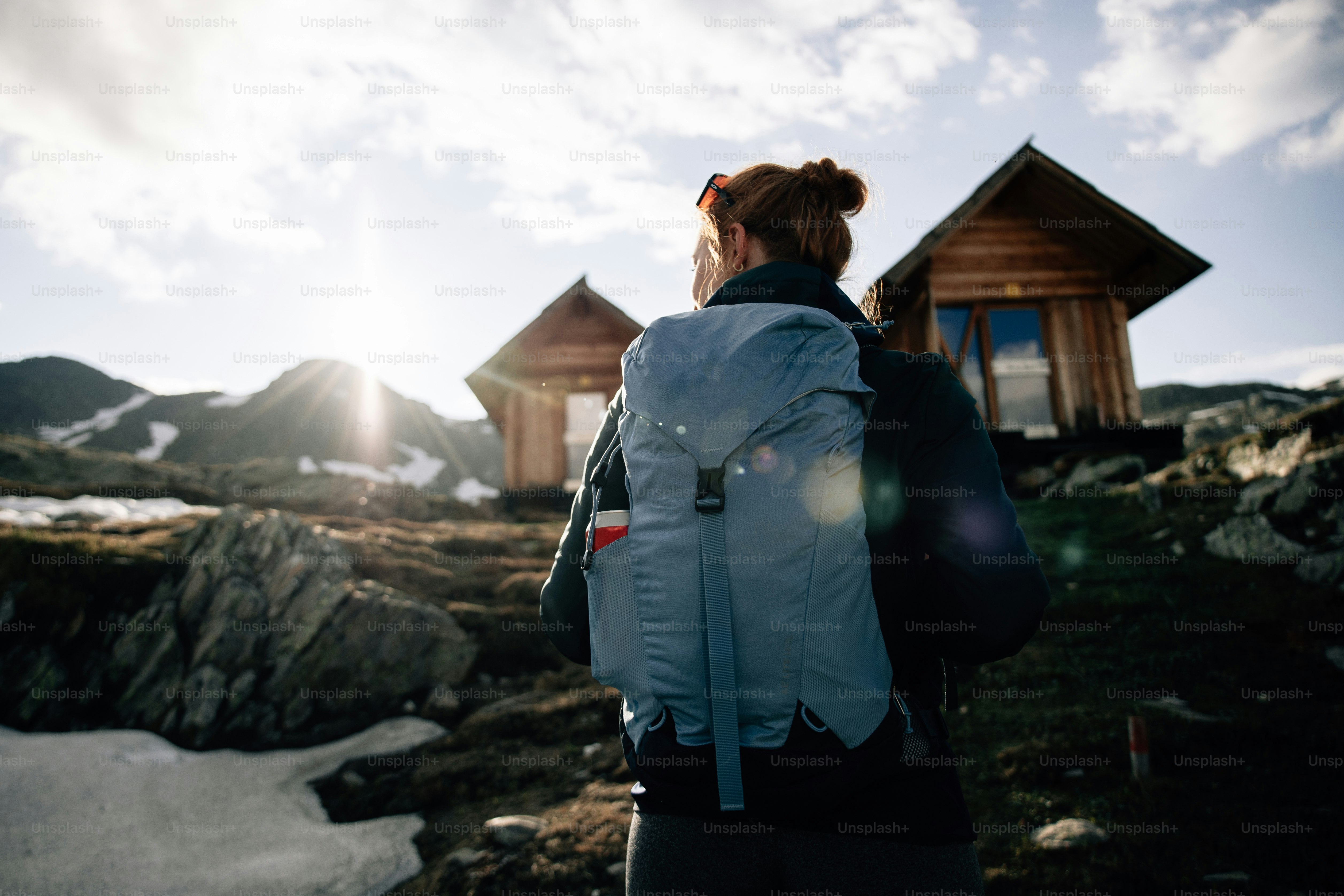Hiker with backpack viewing mountain cabins at sunset.