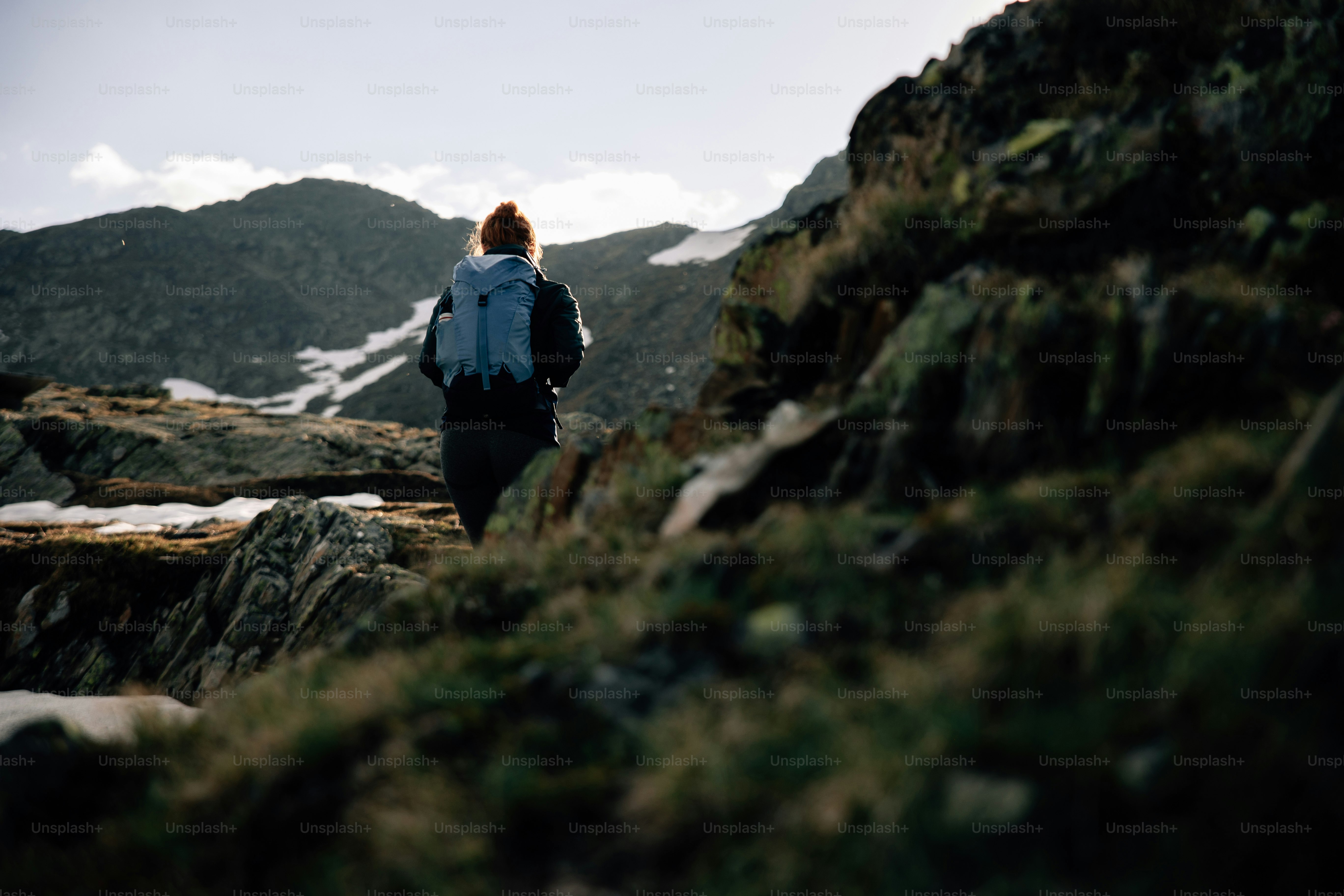 A person hiking through rocky mountains under a bright sky.