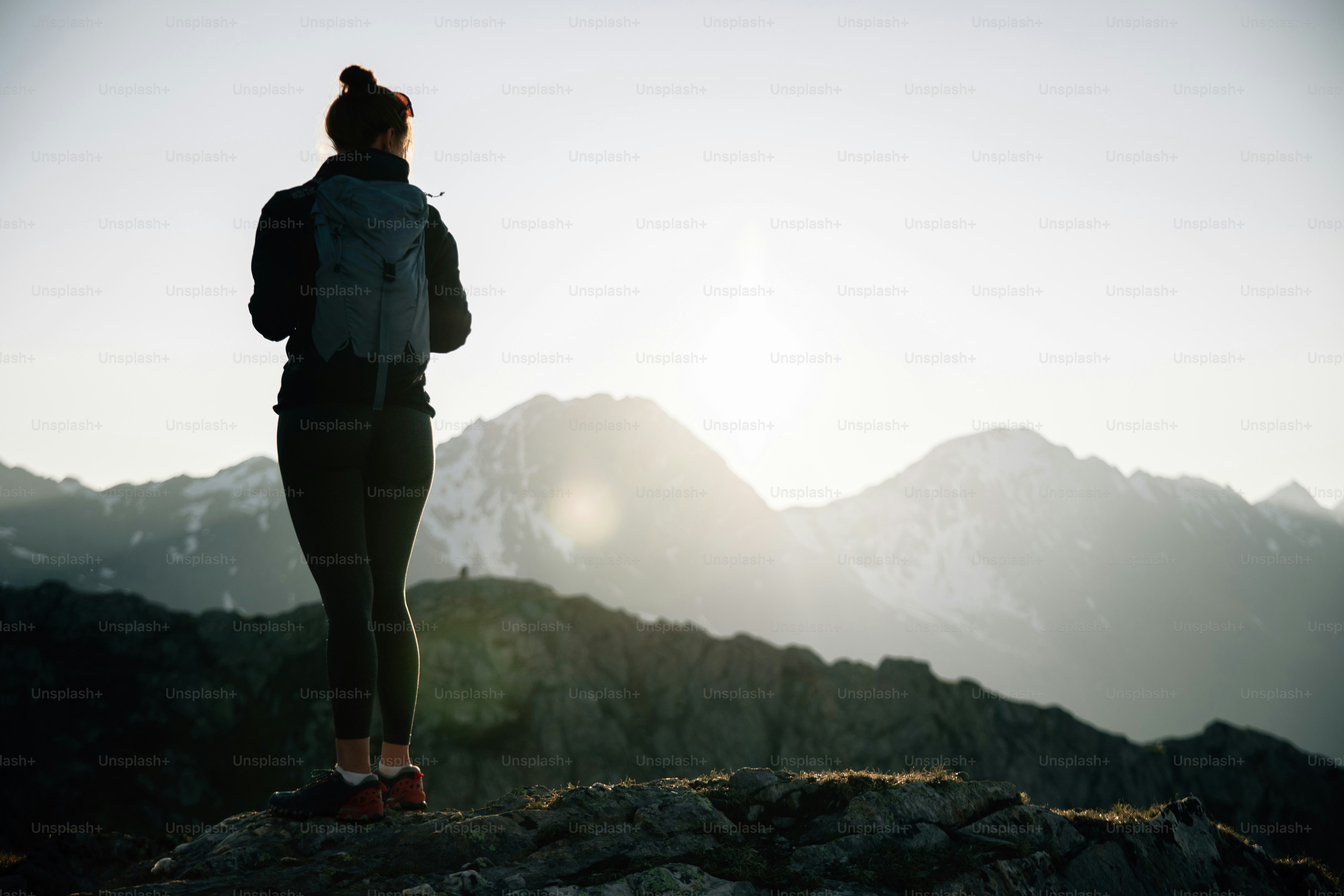Bei Sonnenaufgang steht eine Person auf einem Berggipfel