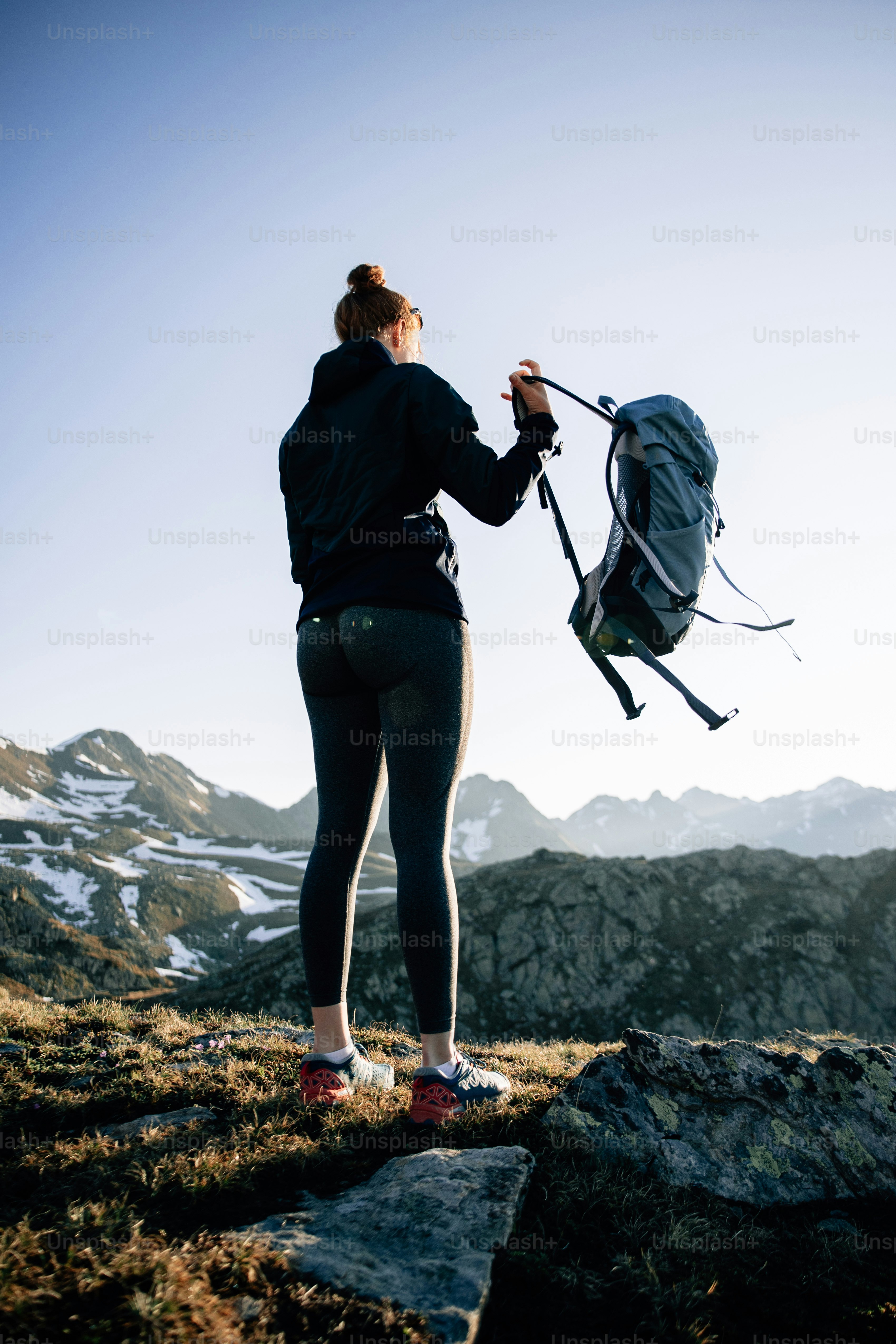 Pendaki memegang ransel di puncak gunung saat matahari terbit.