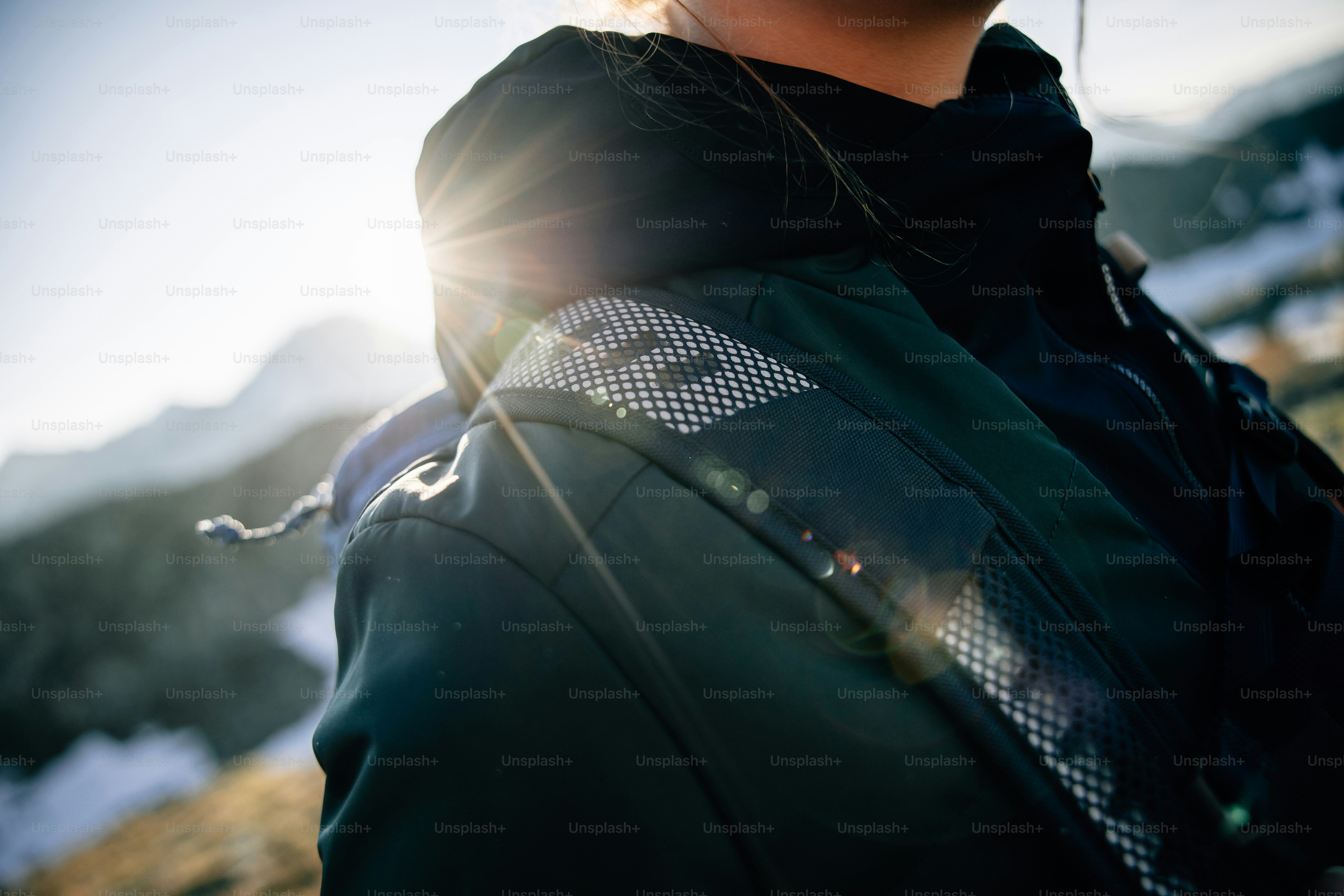 Sunlight flares over a person's reflective jacket in mountains.