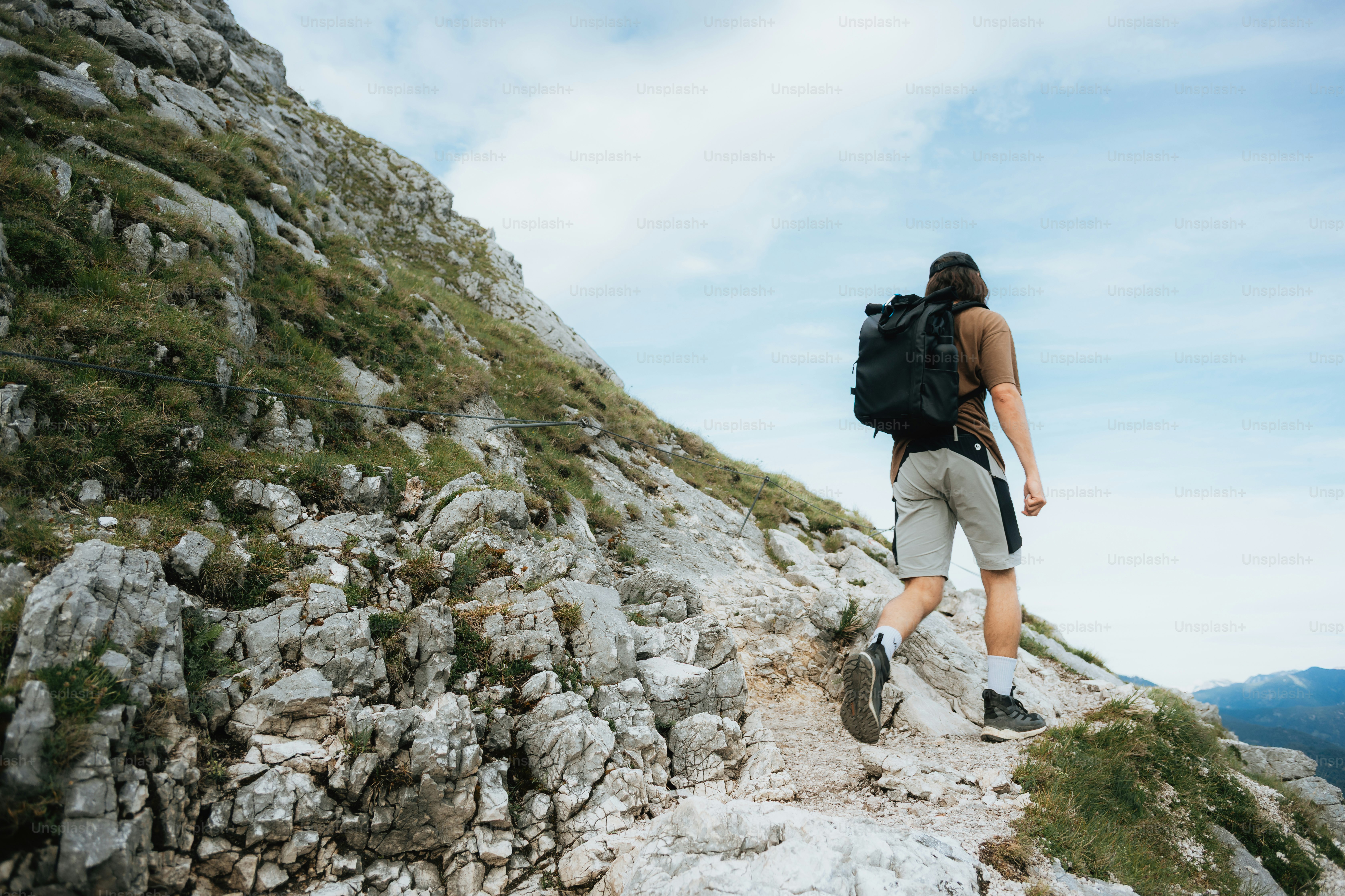 Mann mit Rucksack steigt einen steilen Bergpfad hinauf