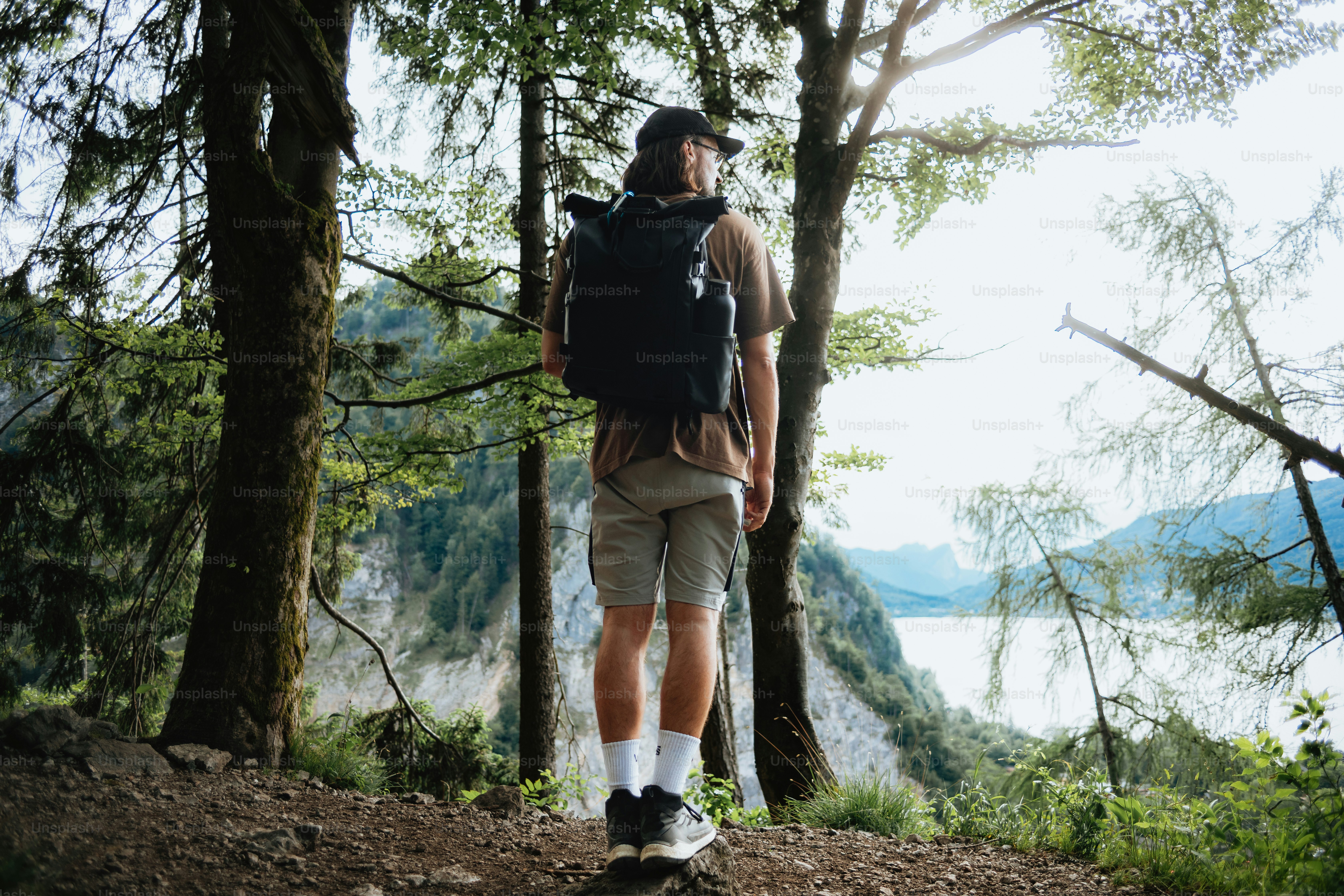 Pendaki dengan ransel berdiri di hutan yang menghadap ke danau yang indah.