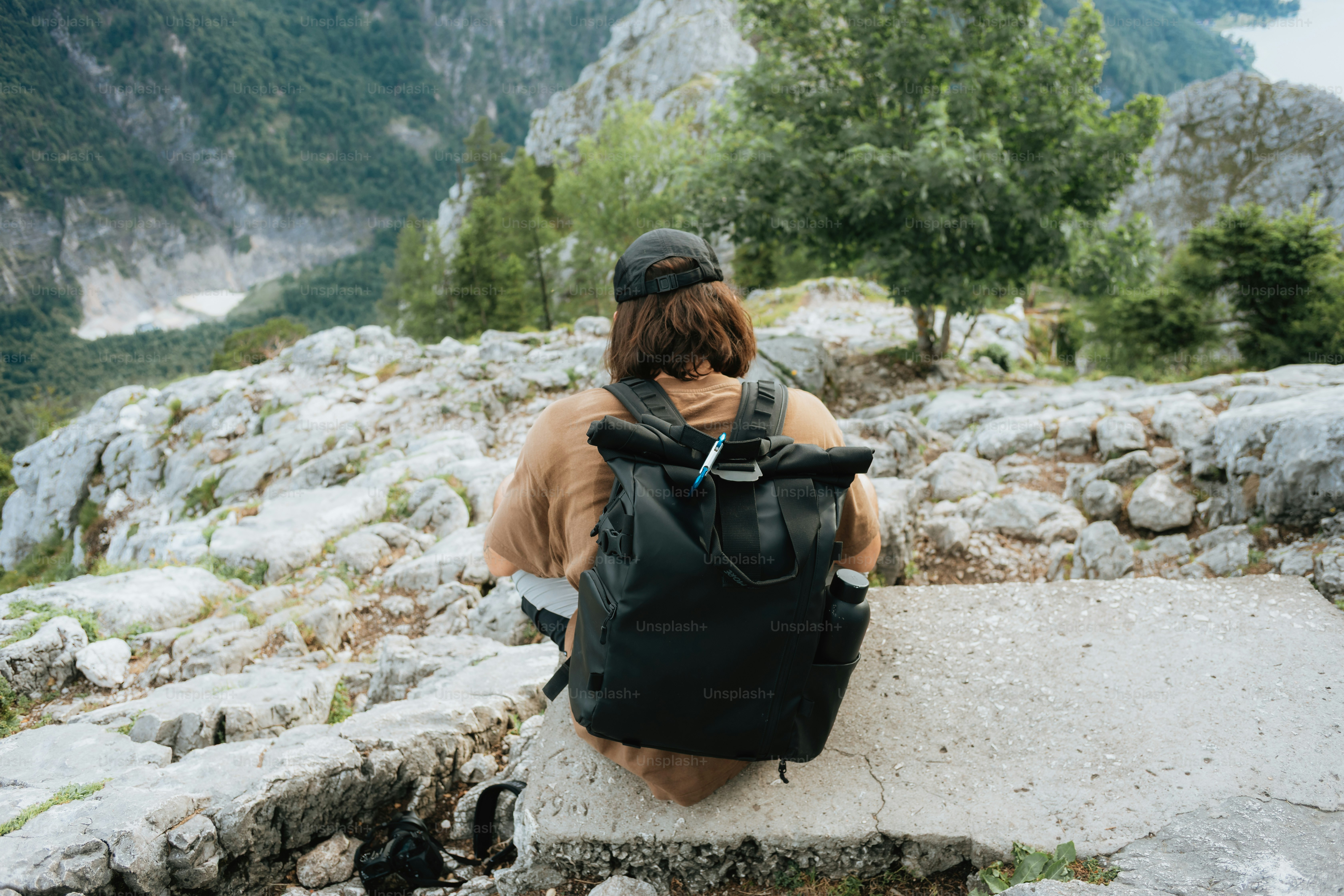 Orang dengan ransel duduk di gunung yang menghadap ke lembah.