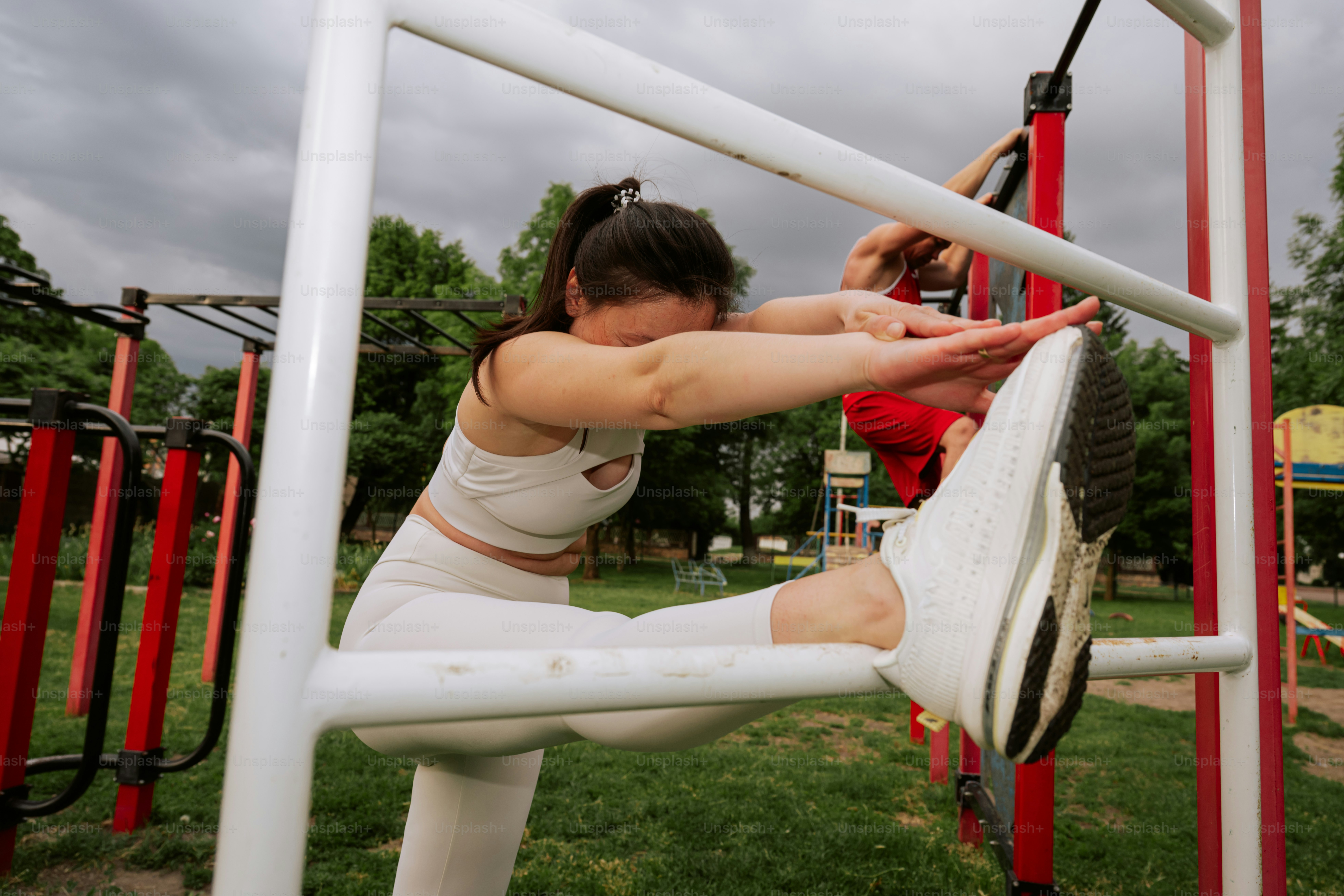 Woman stretches her leg on a white outdoor gym bar