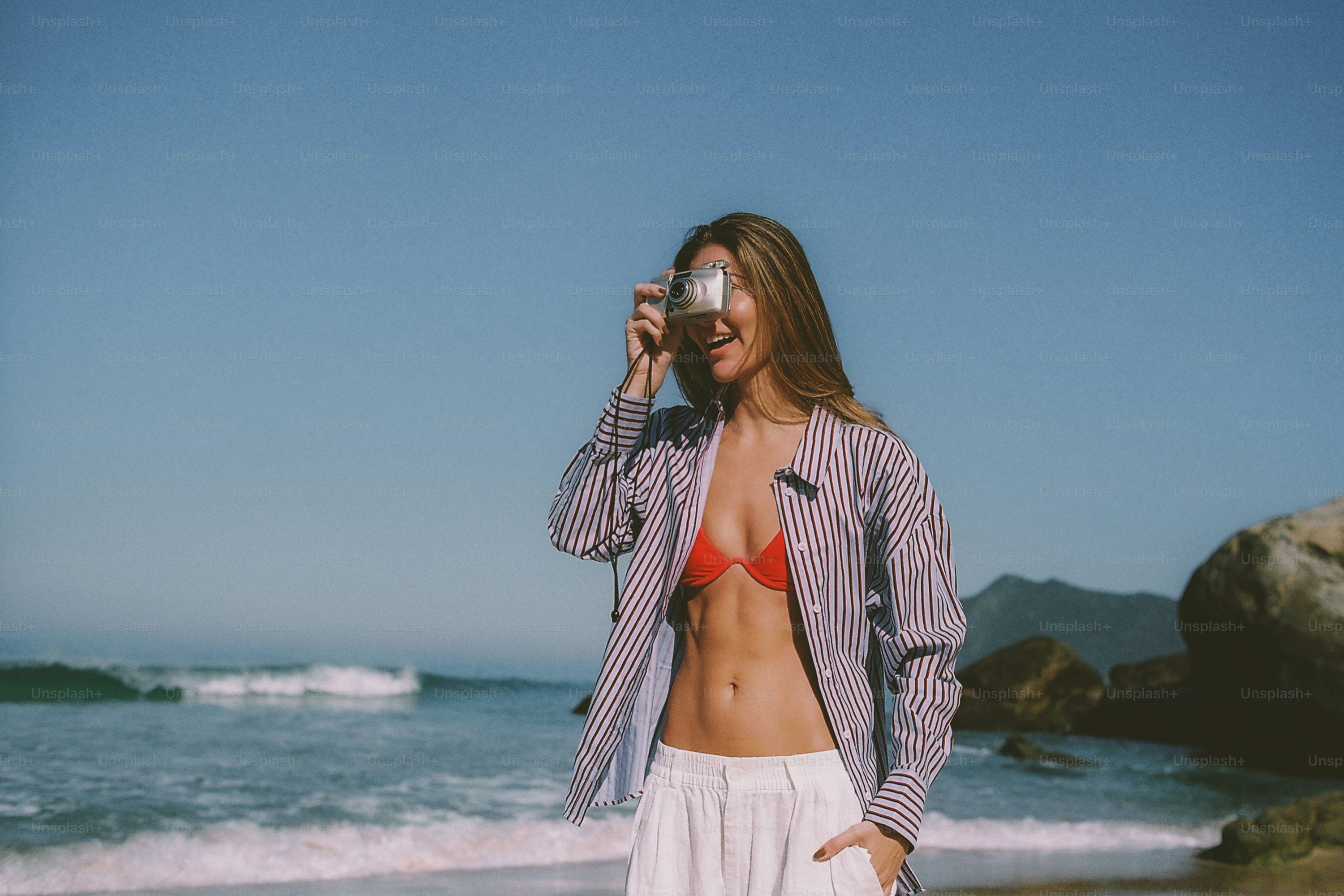 A woman taking a picture on a sunny beach.