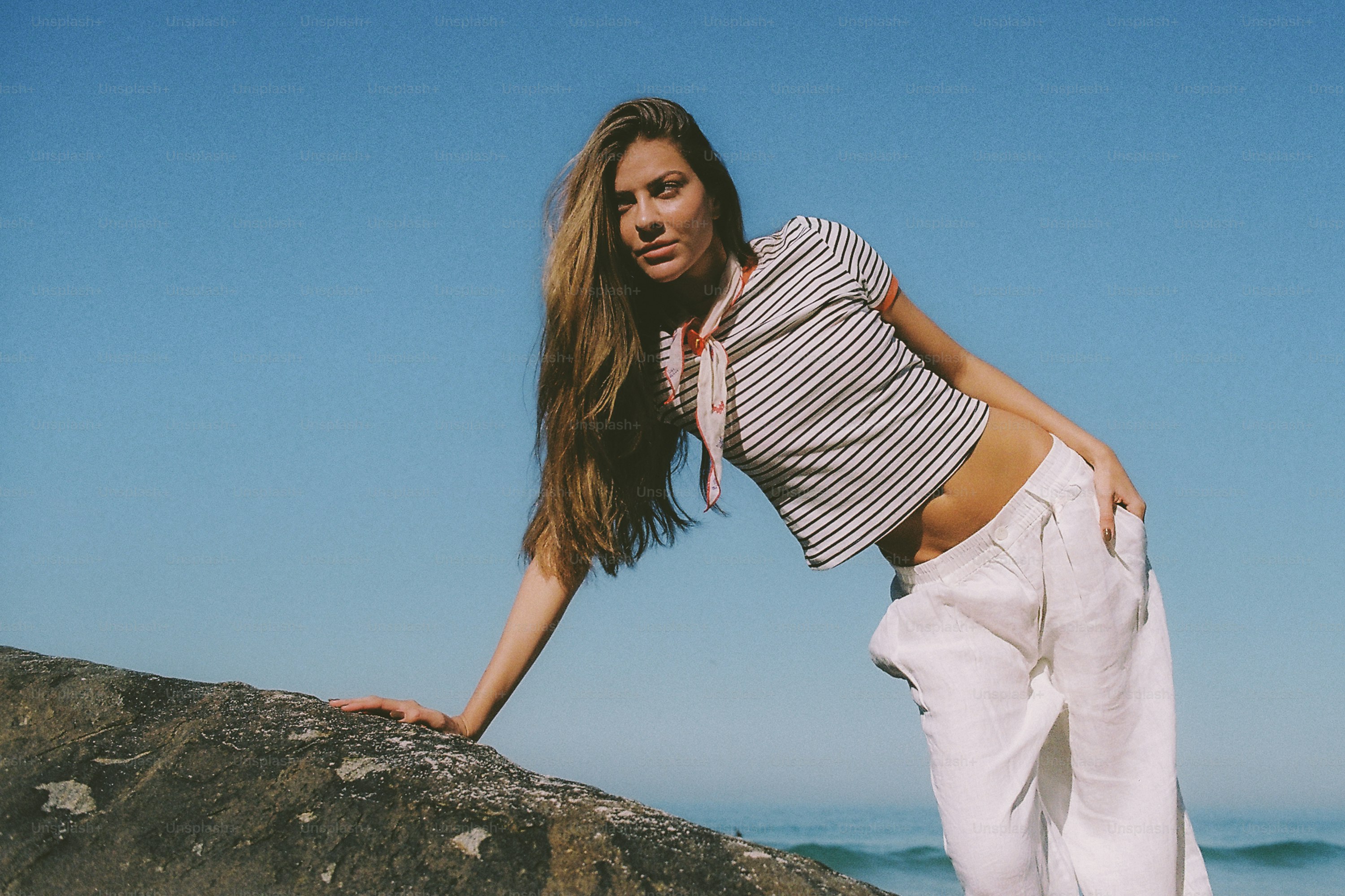 Young woman leaning on a rock by the ocean.