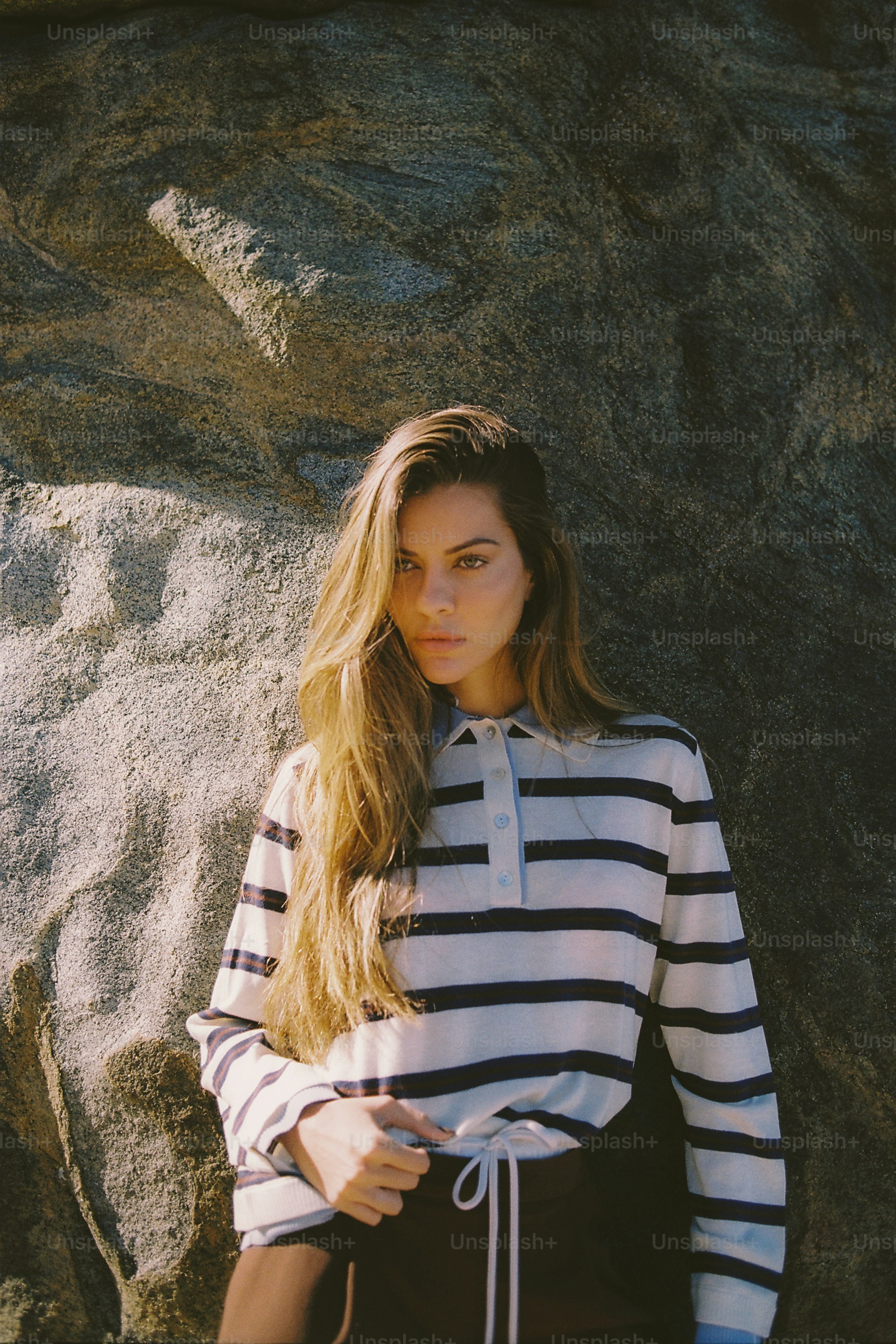 Woman in striped shirt poses against a large rock.