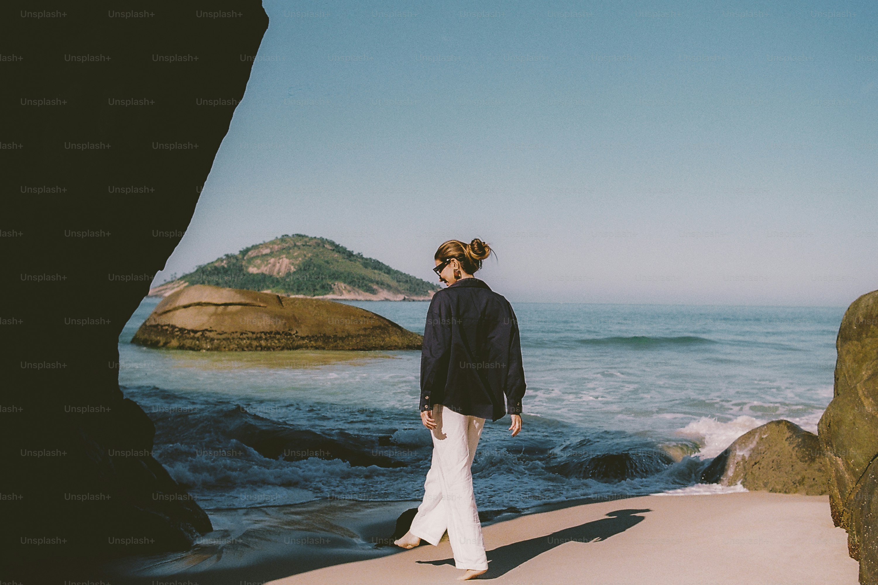 Woman walking on a beach with ocean and distant island.