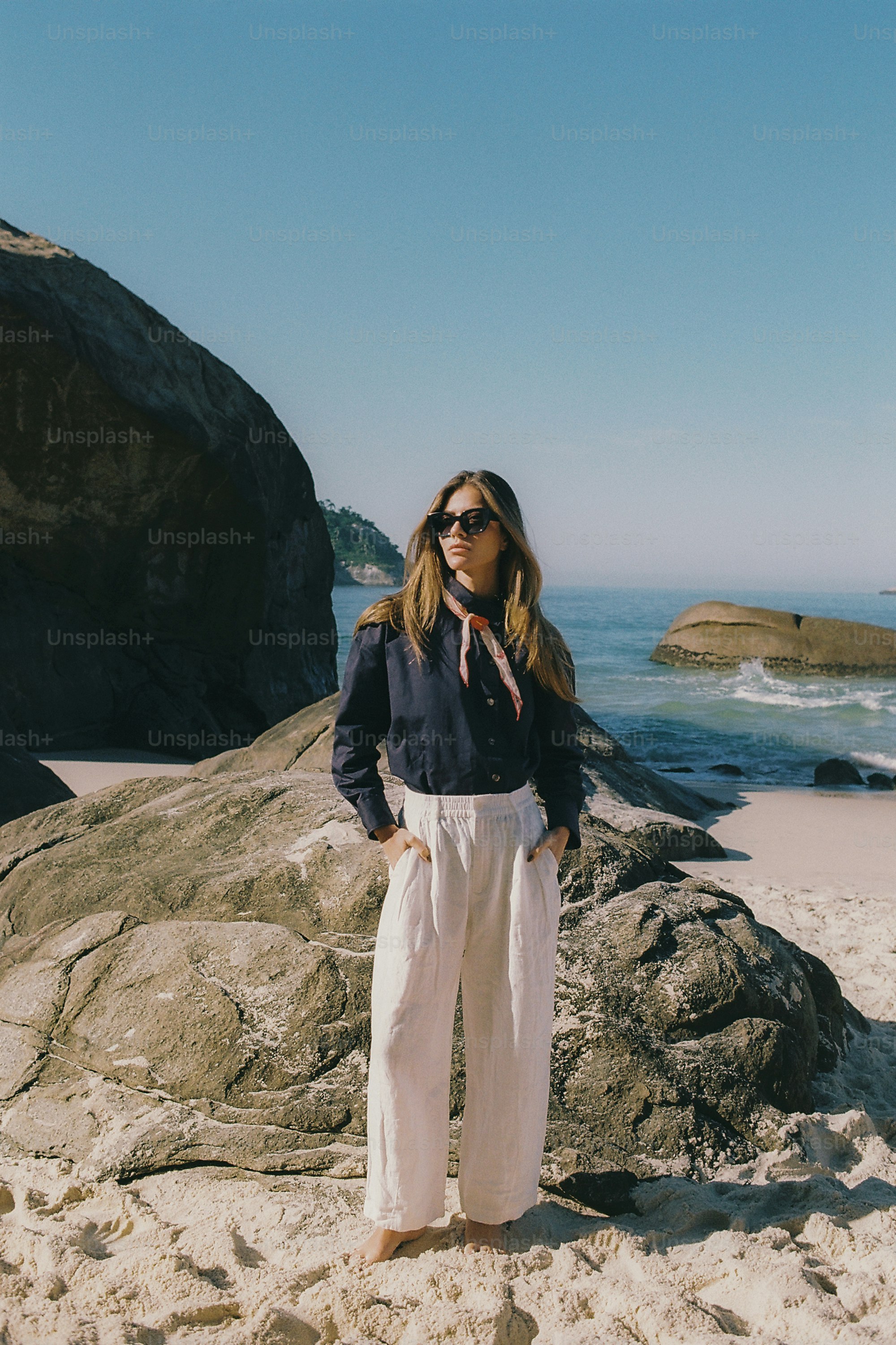 Stylish woman on a sunny beach with large ocean rocks.