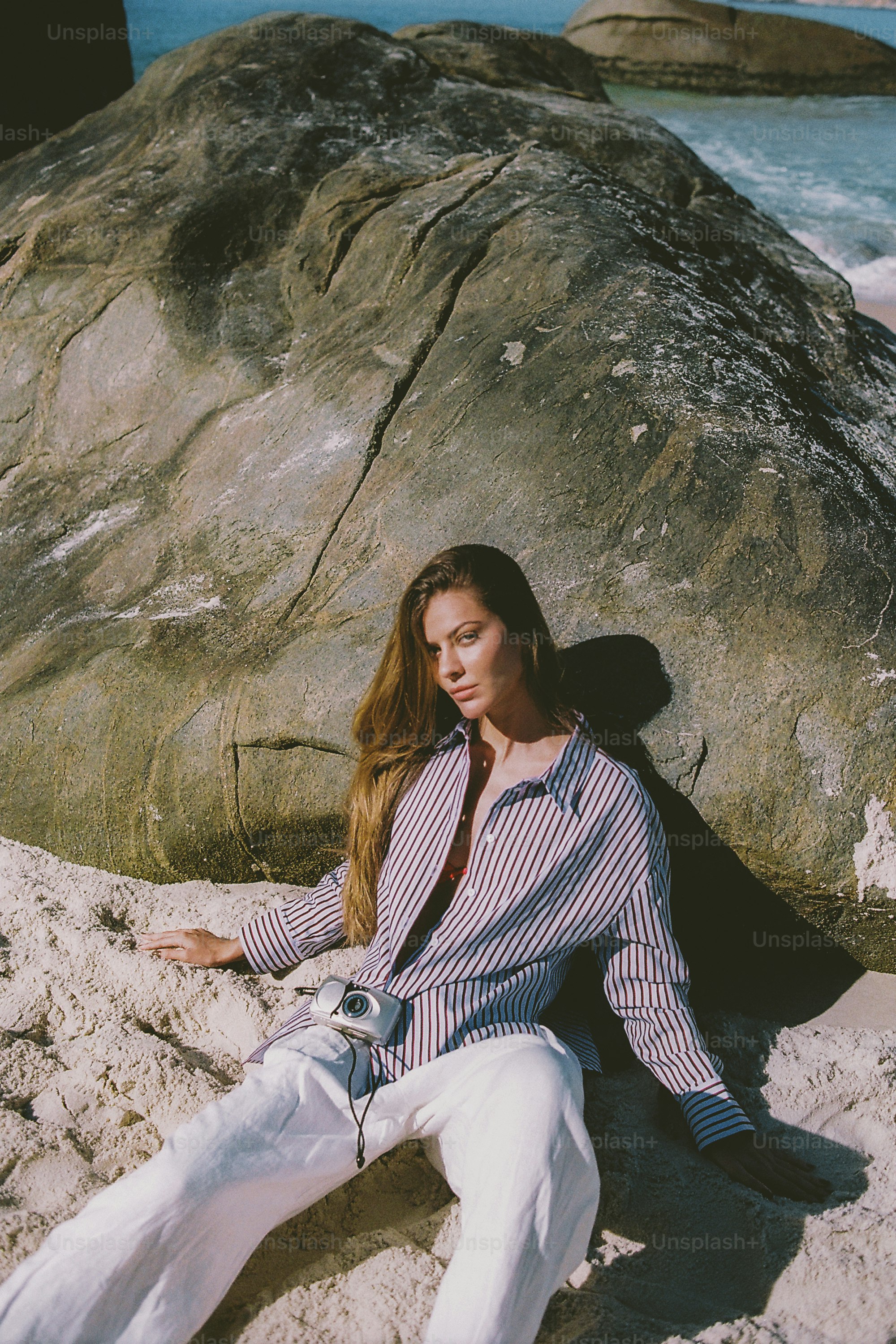 Woman leans against large rock on a sunny beach.