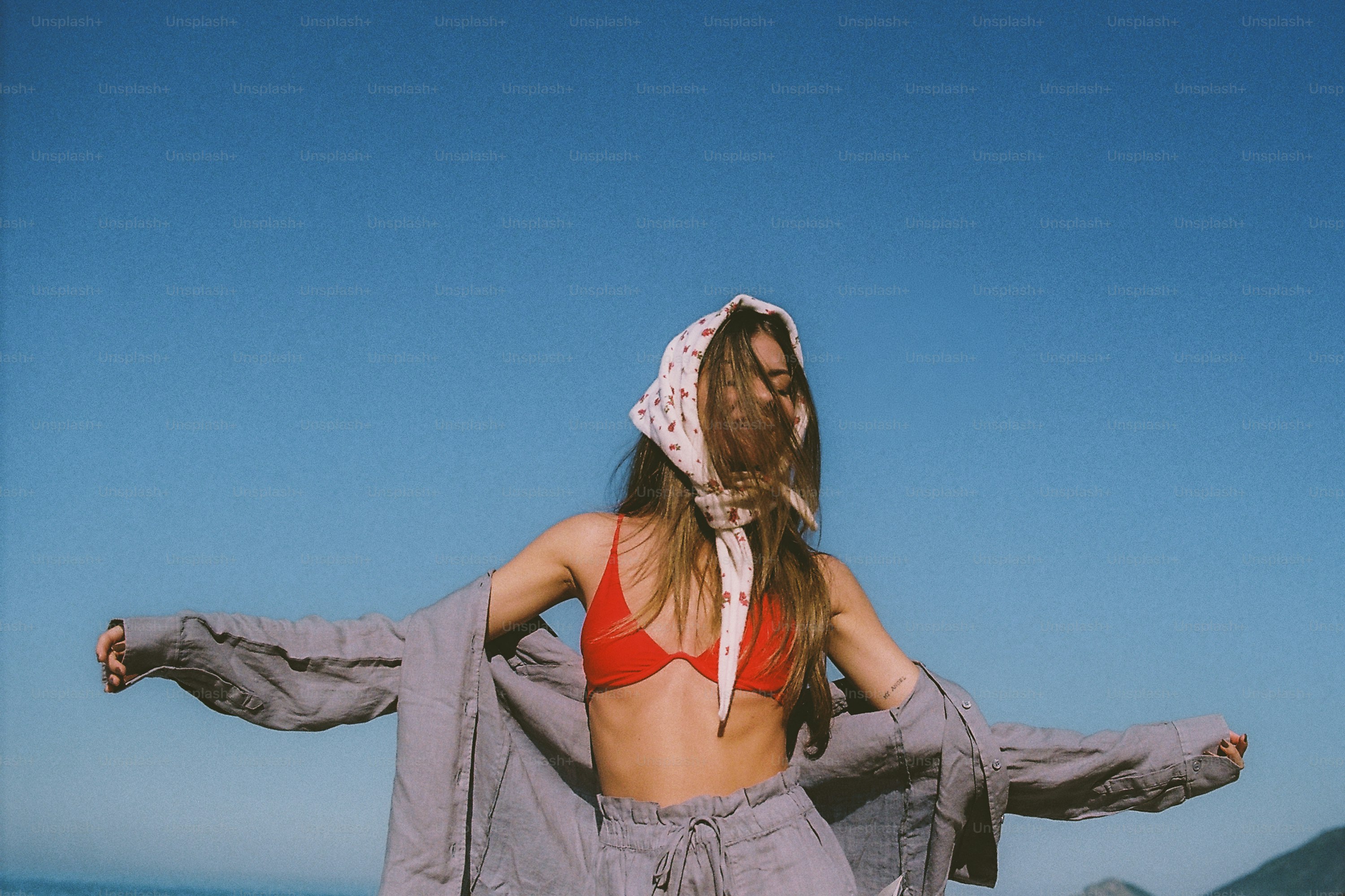 Young woman in red bikini and headscarf with arms outstretched.